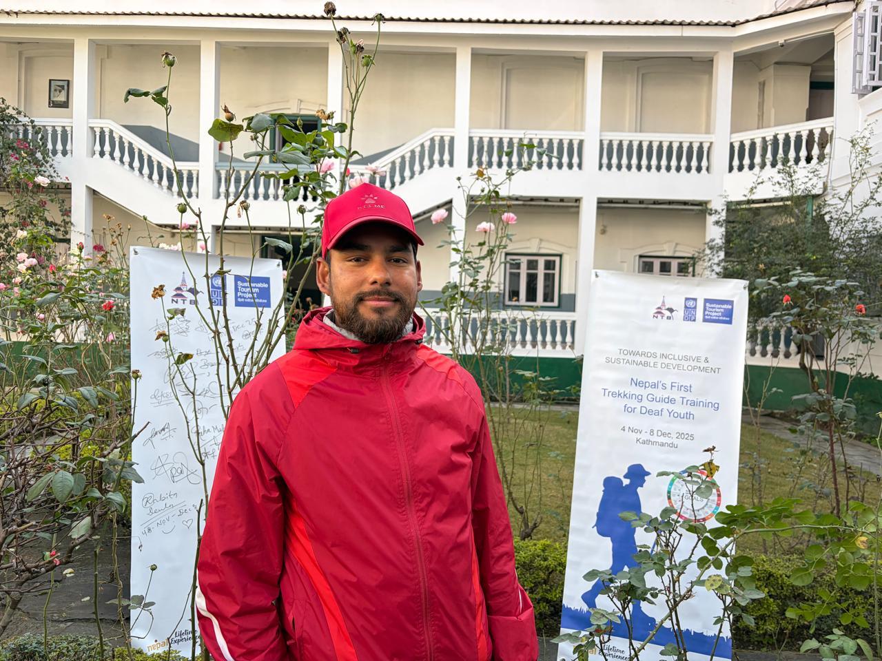 Person in red jacket stands outdoors in front of banners beside a white building.