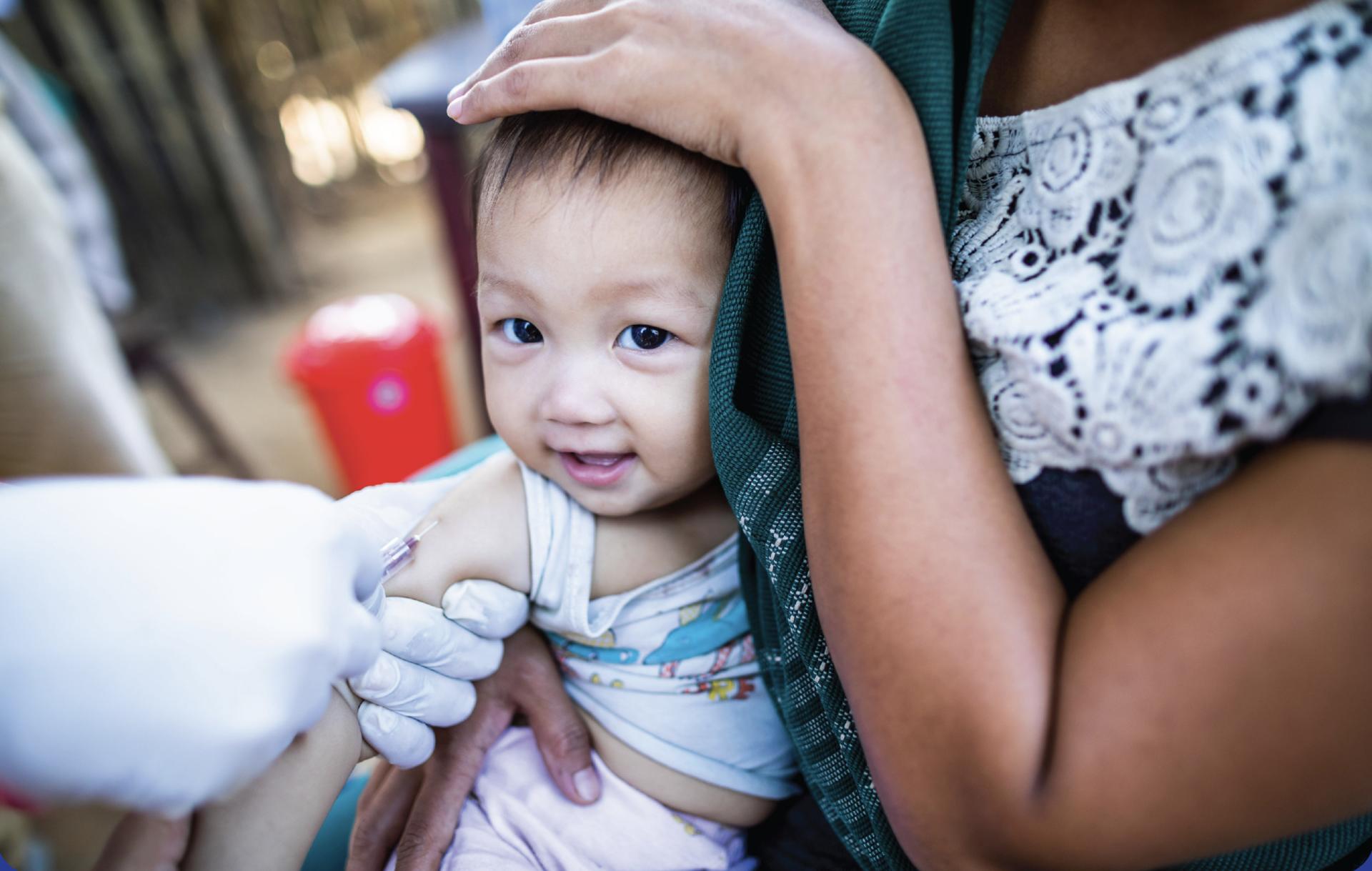 Healthcare worker's gloved hand administers a vaccine to a child's arm.