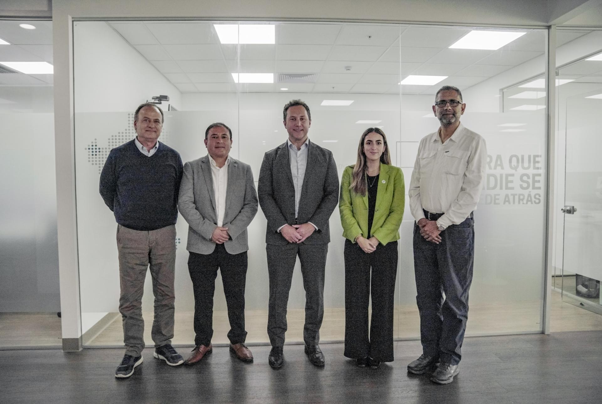 Five professionals stand in a glass-walled office lobby posing for a group photo.
