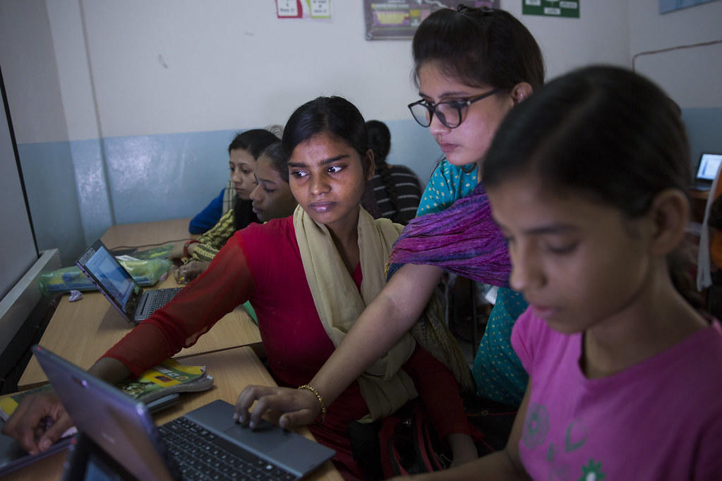 Group of students around laptops in a blue-walled classroom.