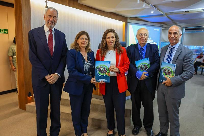 Six professionals in business attire pose indoors, some holding green books.