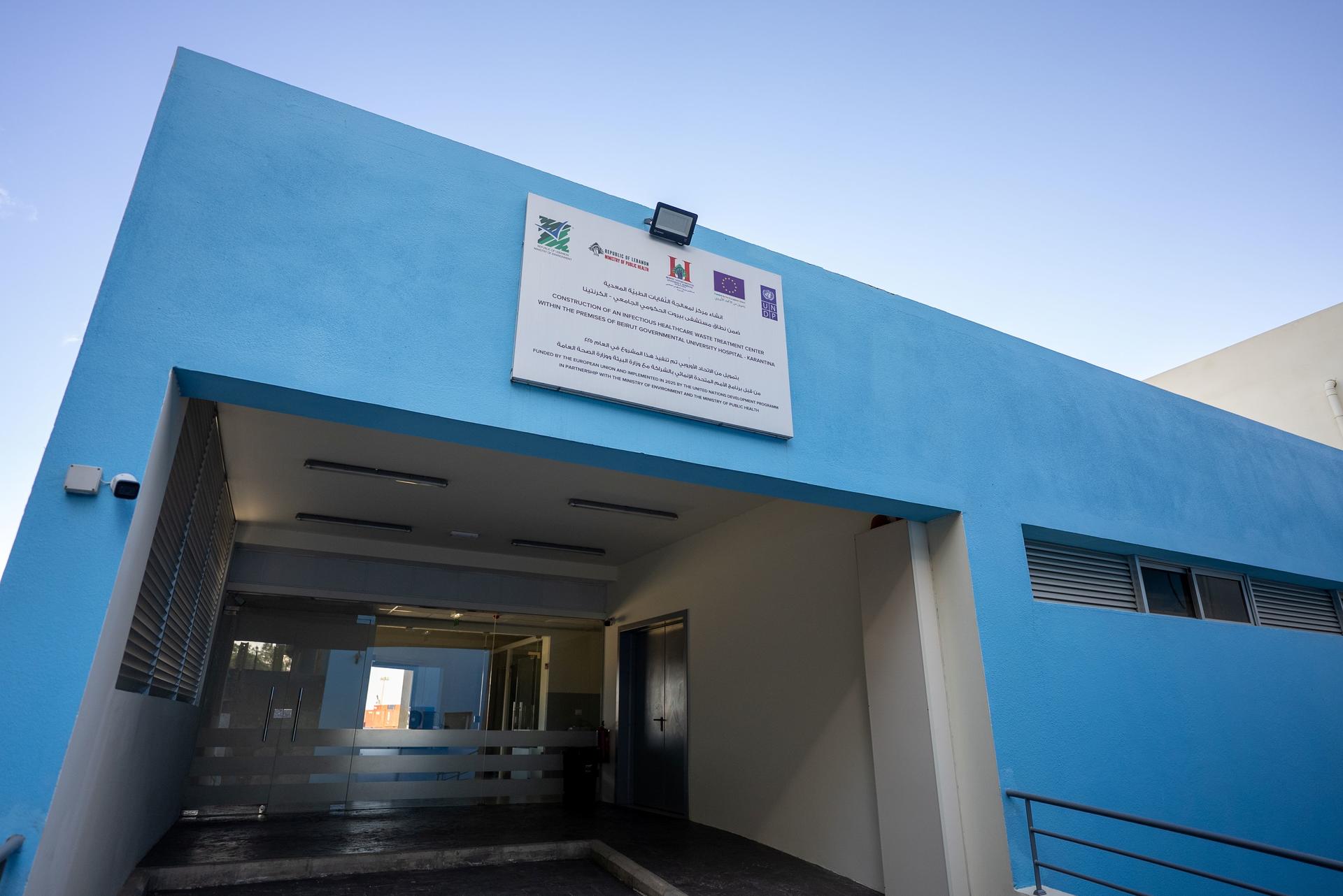 Blue building with a covered entrance and a signboard above under a clear sky.
