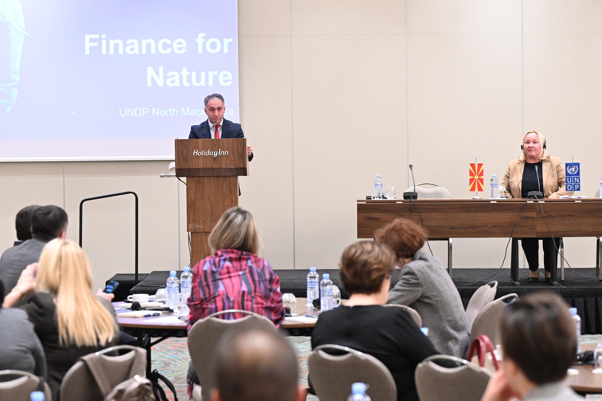 Speaker at podium addressing audience at Finance for Nature conference; panelists at table.