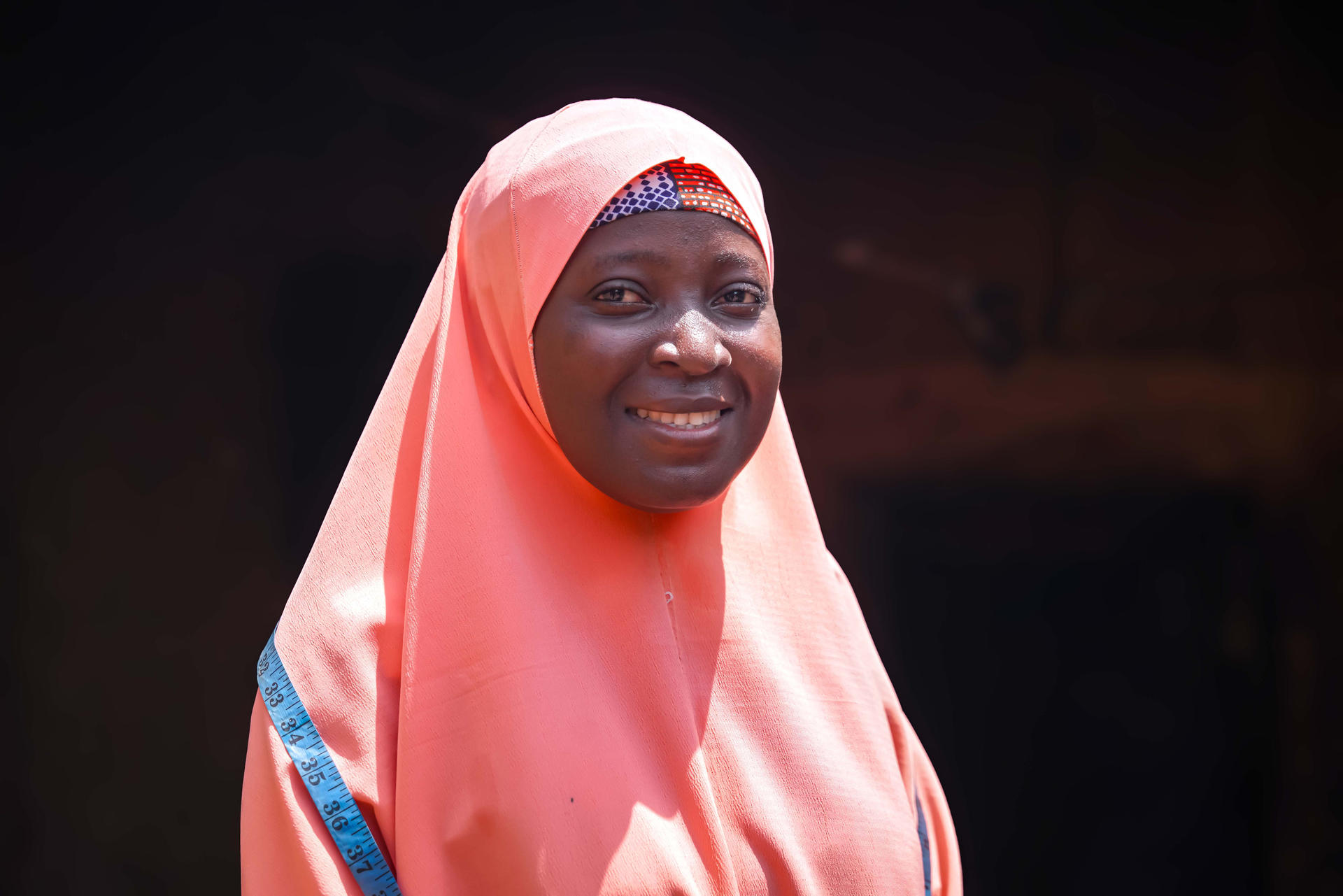 Person wearing pink hijab with blue trim against a dark background.