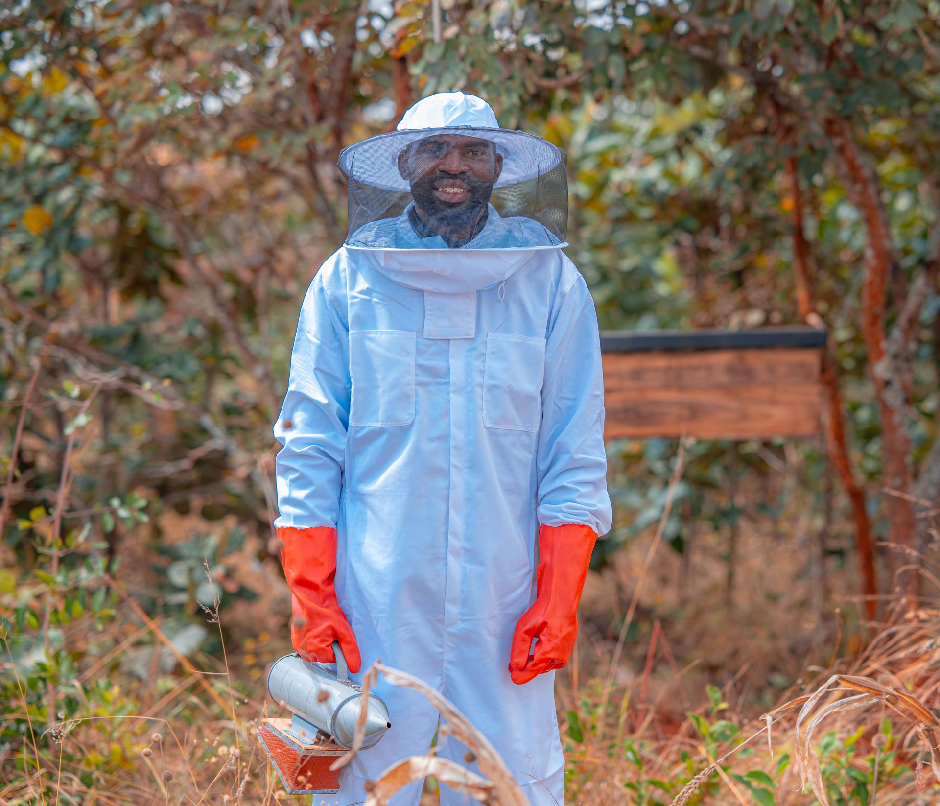 Person in blue hazmat suit and red gloves standing in a forest, holding a spray device.
