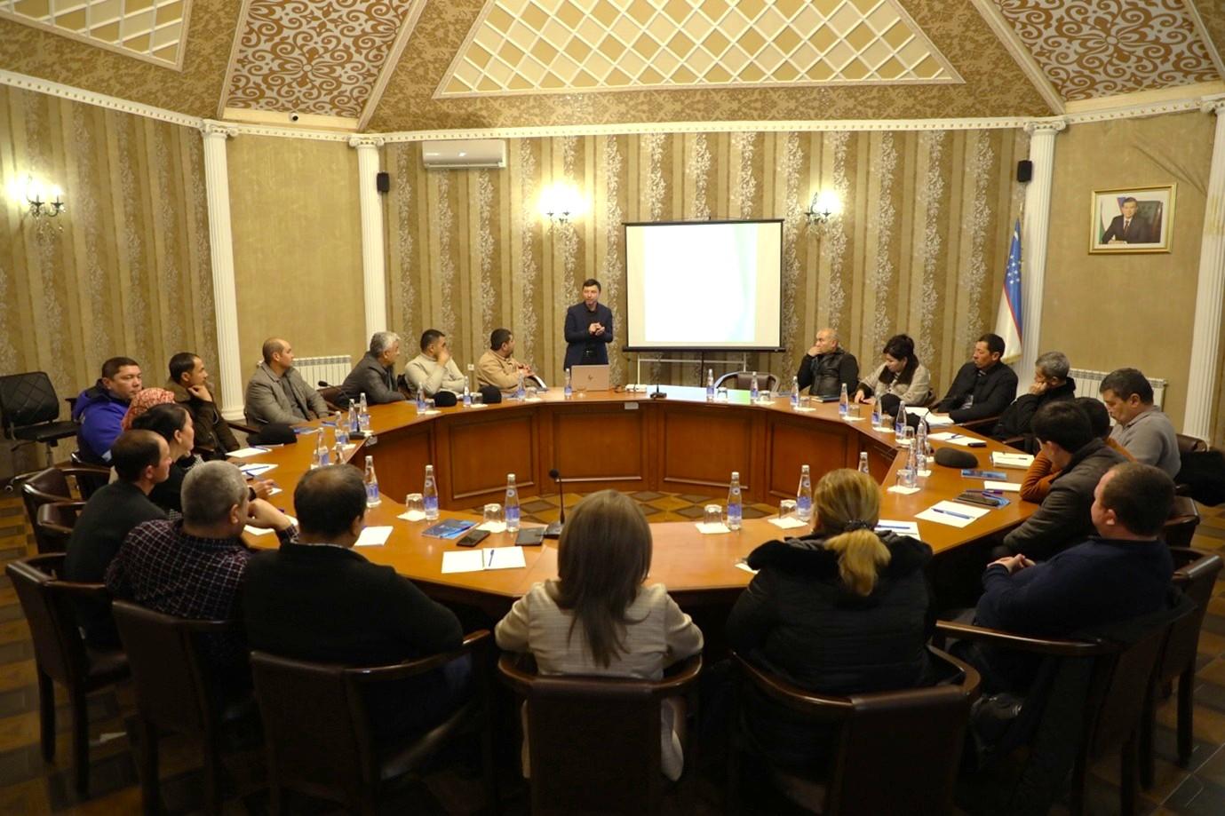 Photograph of people seated around a large round conference table in a formal meeting room.