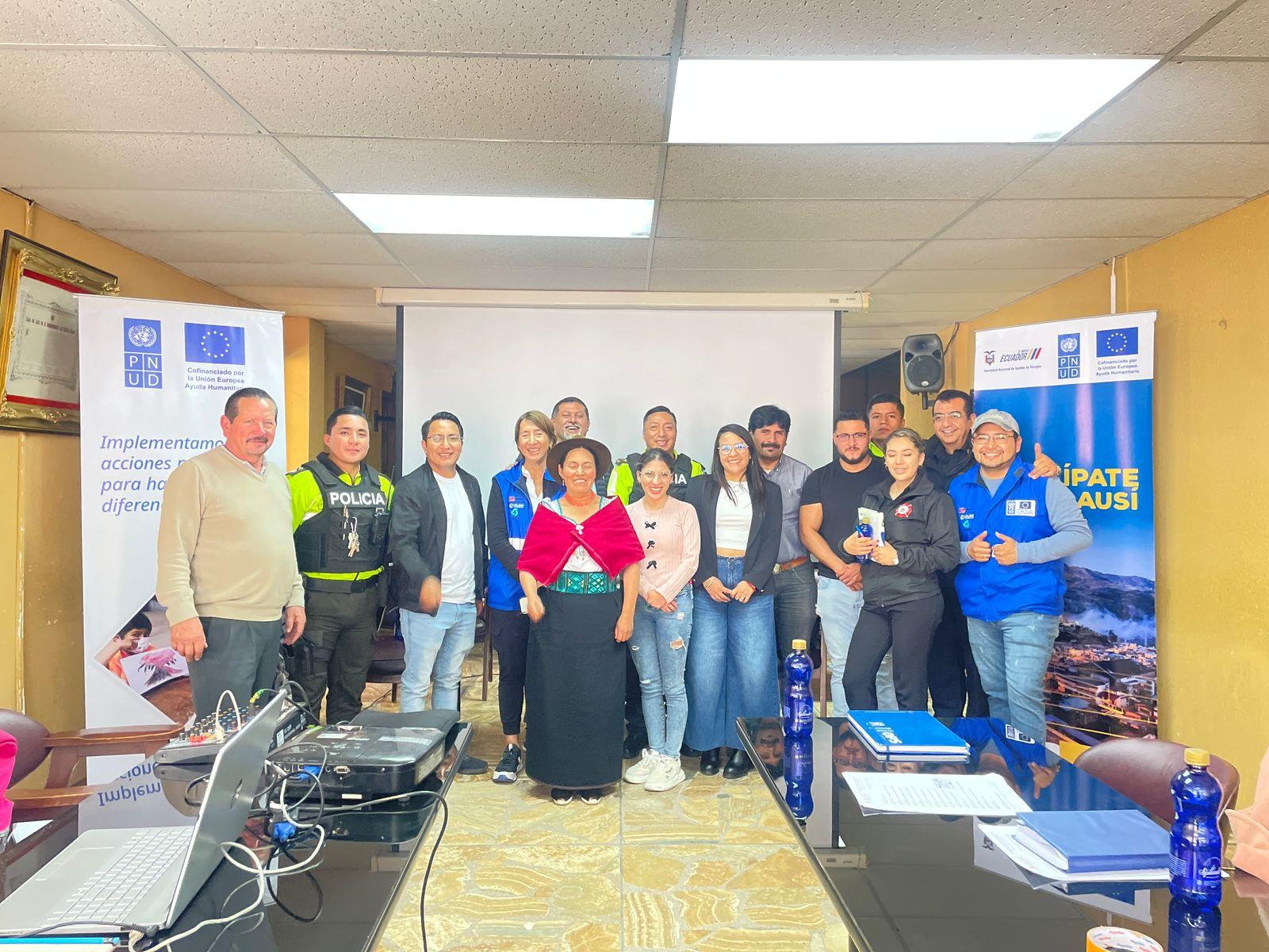 Group of people posing for a workshop photo in a classroom with laptops and banners.
