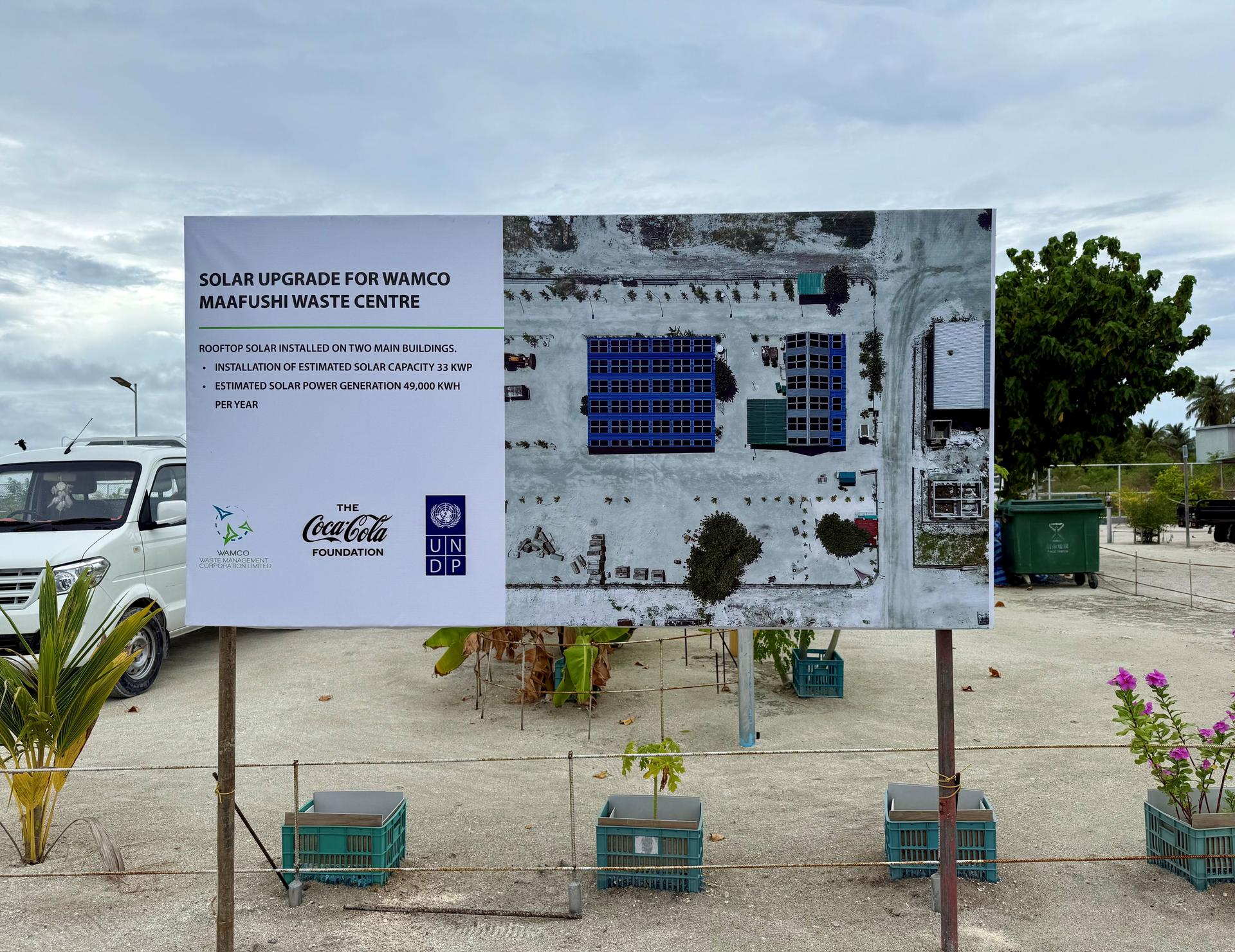 Outdoor information board with solar diagrams and photos; green equipment crates and a car nearby.
