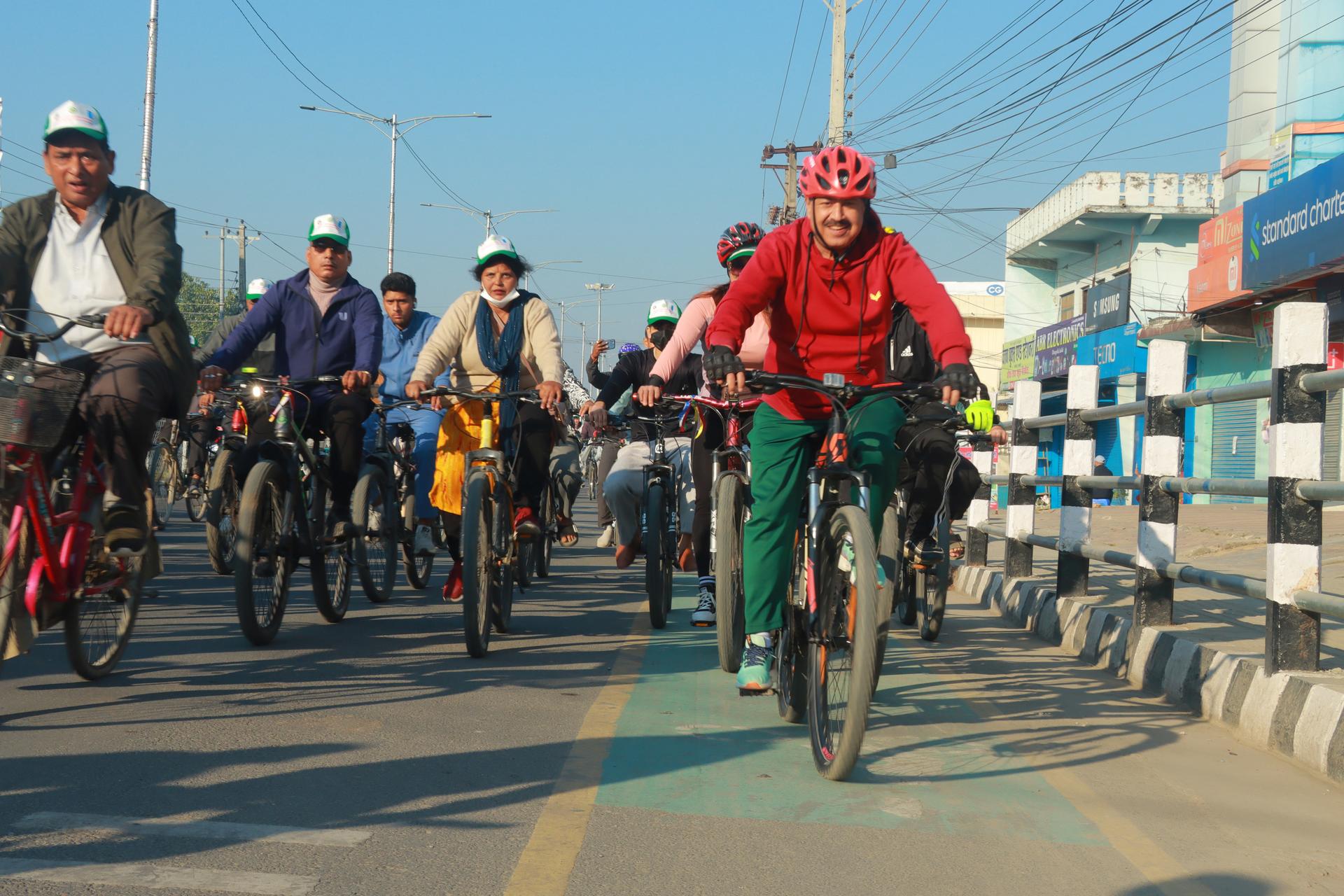 Photograph of cyclists riding on a city bridge; foreground rider wearing a red shirt.
