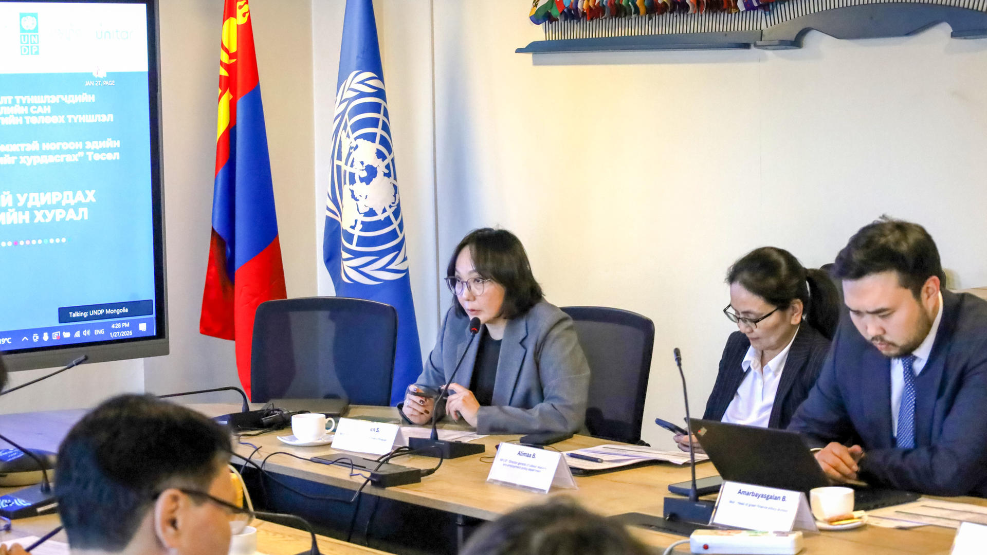 Officials sit around a conference table with Russian and UN flags and a projector screen.