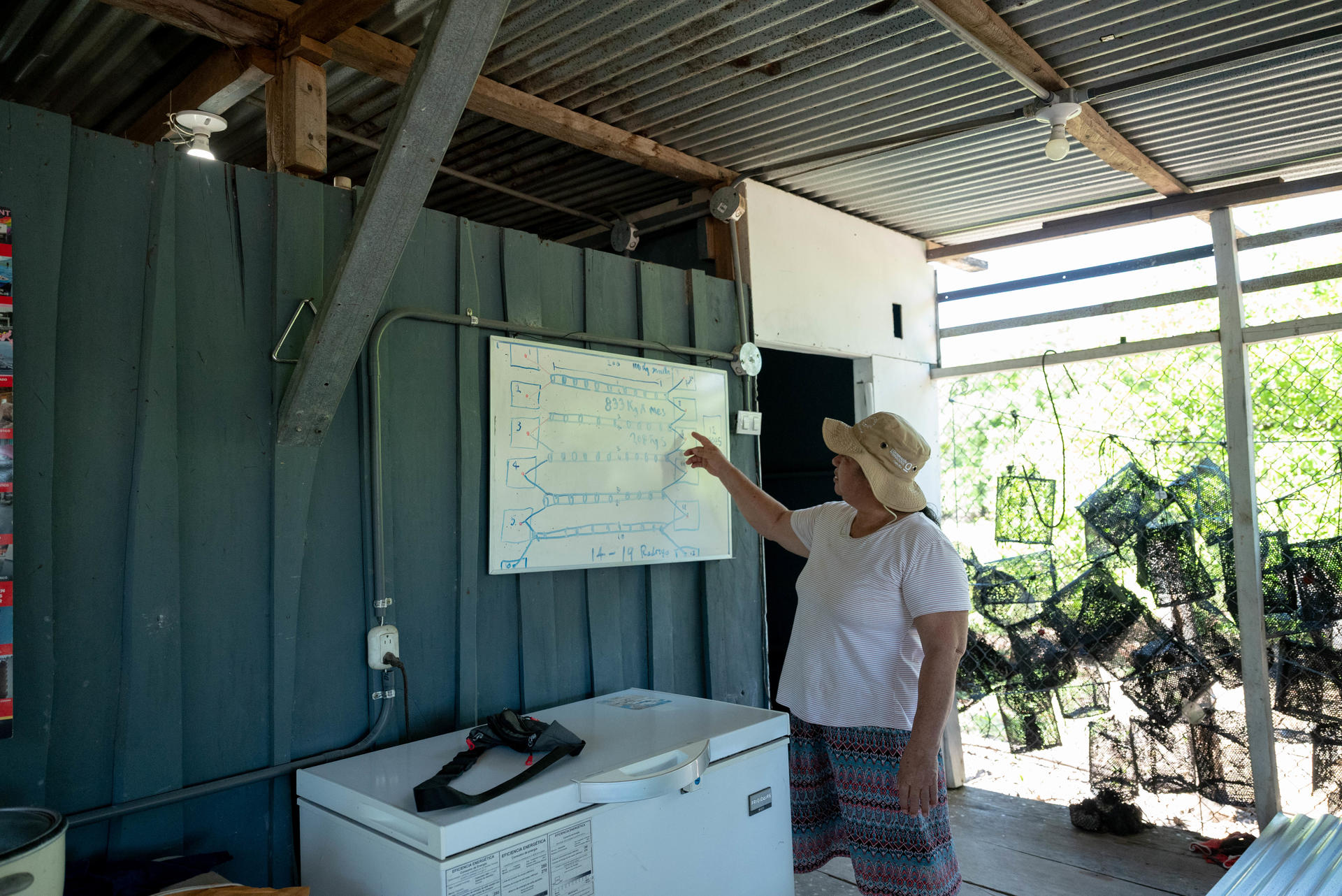 Photo of a woman pointing at a screen in an outdoor classroom under a tin roof.