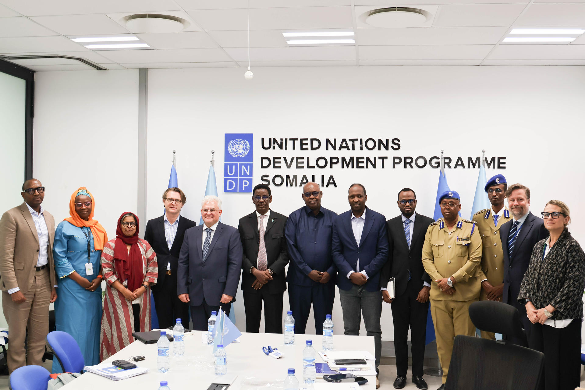 Group photo of officials in a conference room, UNDP sign and flags in background.