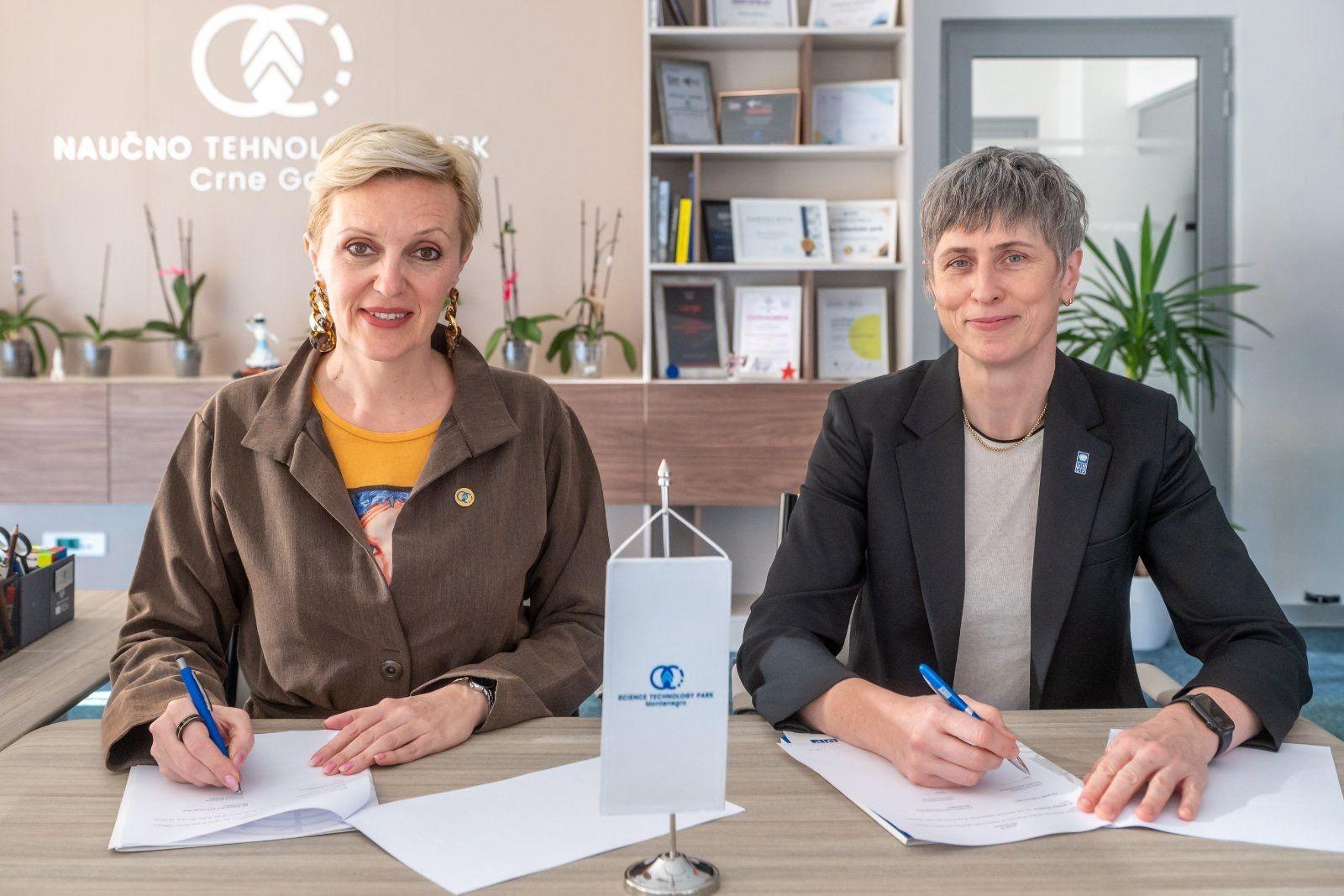 Office scene with two people signing documents at a desk, sanitizer bottle between them.