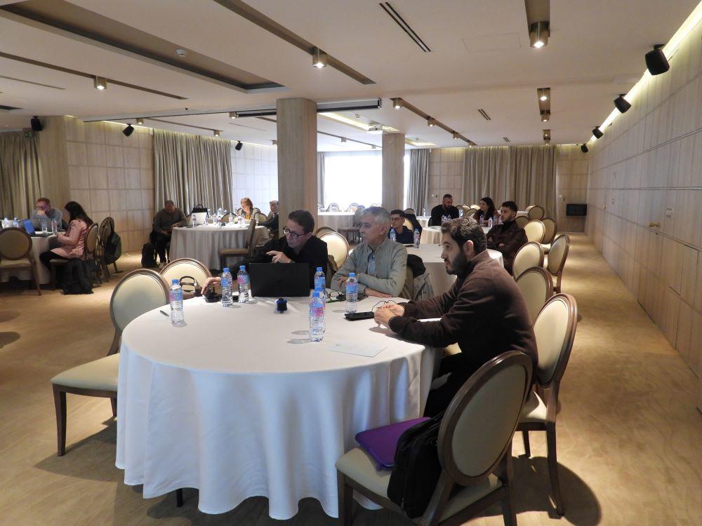 Bright conference room with round tables and attendees seated in groups.