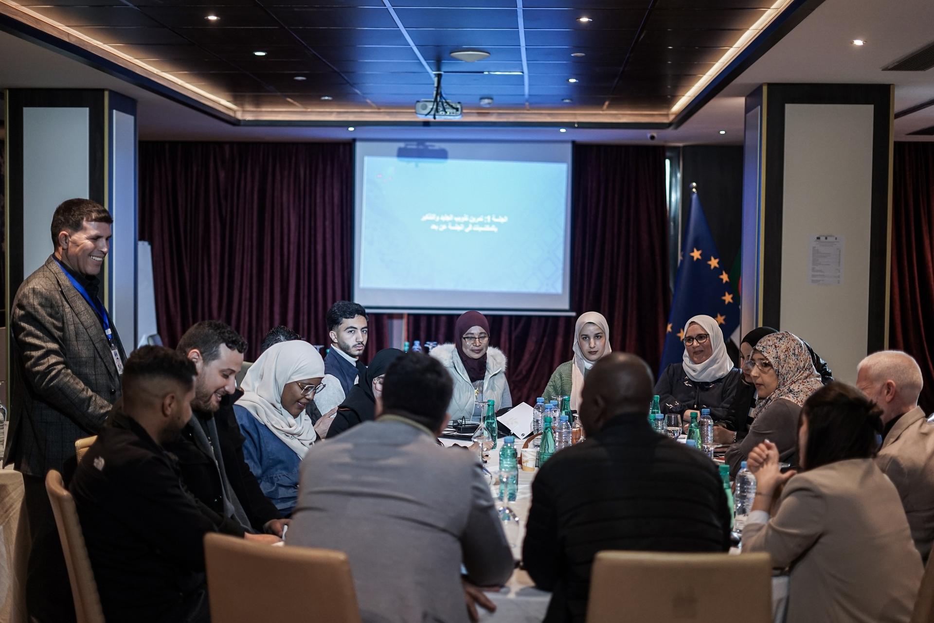 Group of people around a round table in a conference room with a projector screen.
