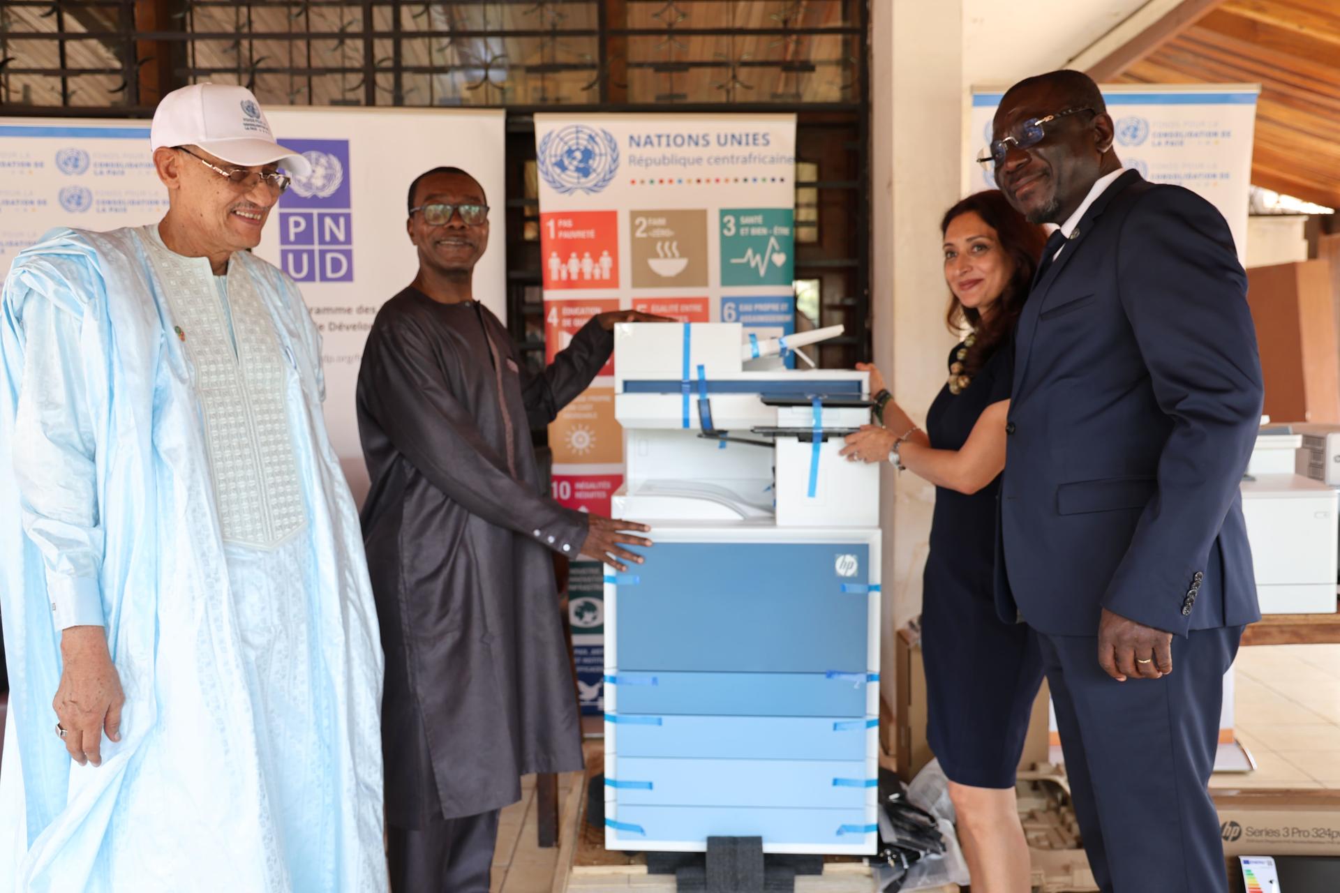 Five people pose beside a blue and white device under a canopy tent.