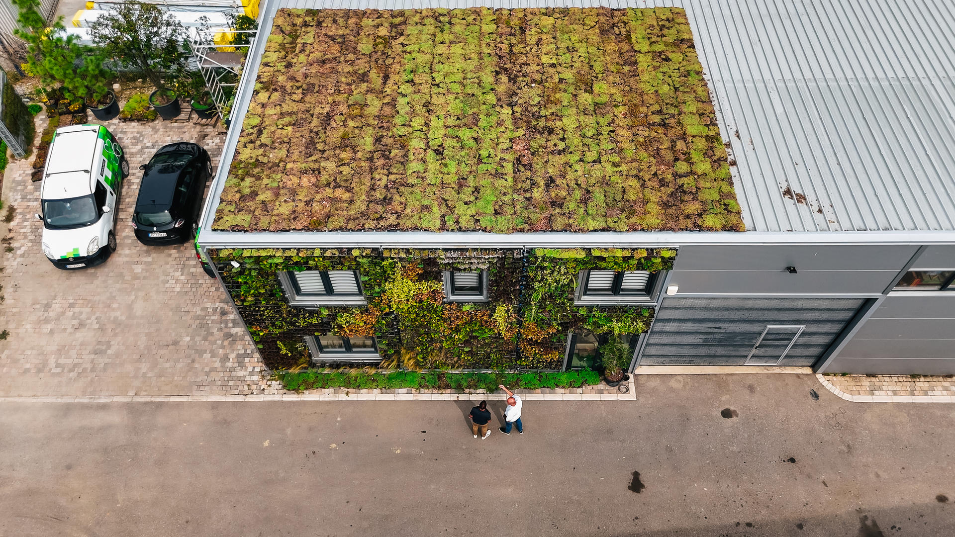 Top-down view of a building with a mossy green roof, green wall, and parked cars.