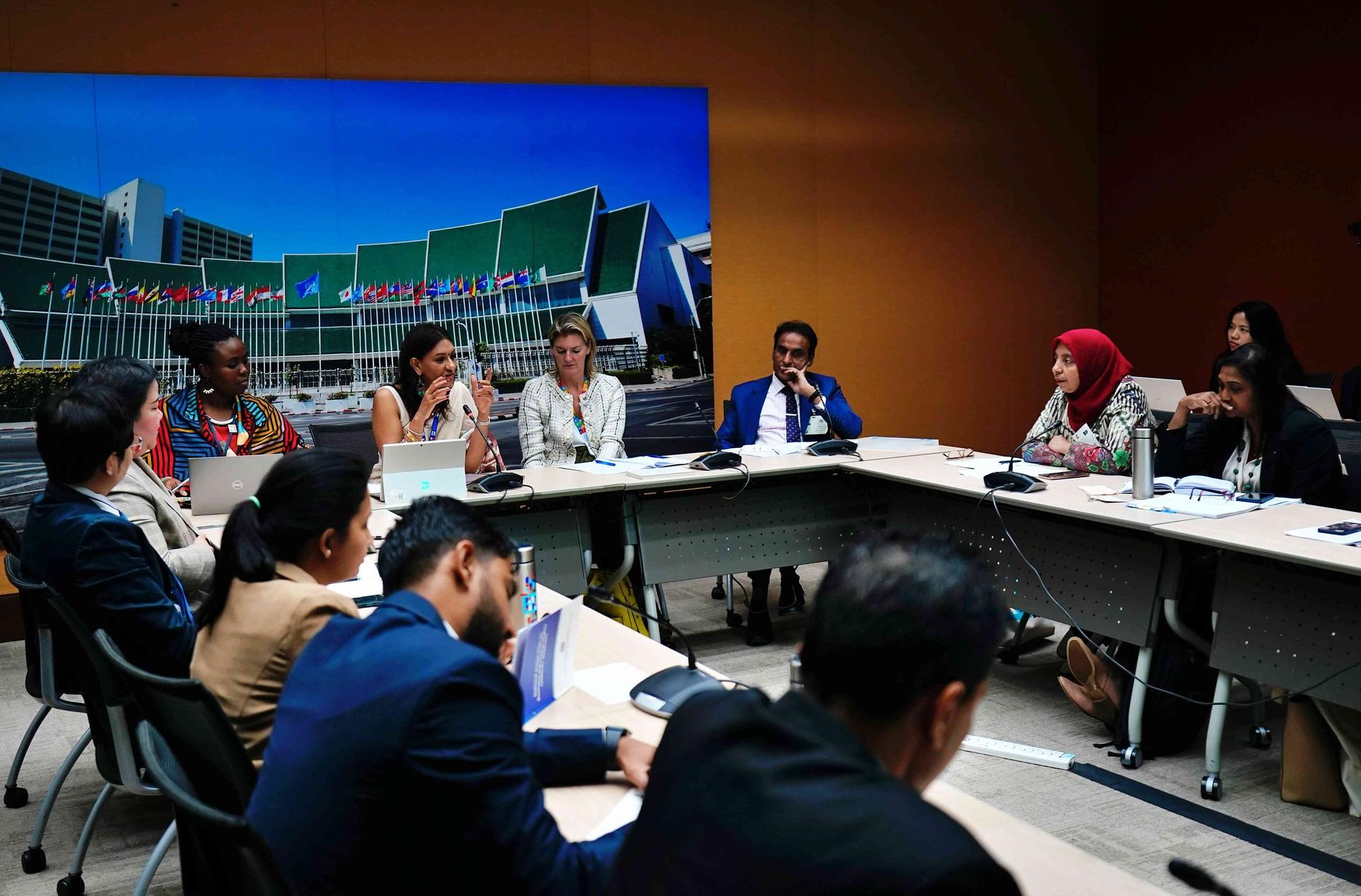 Photograph of a boardroom meeting with people seated along a long table and a cityscape backdrop.