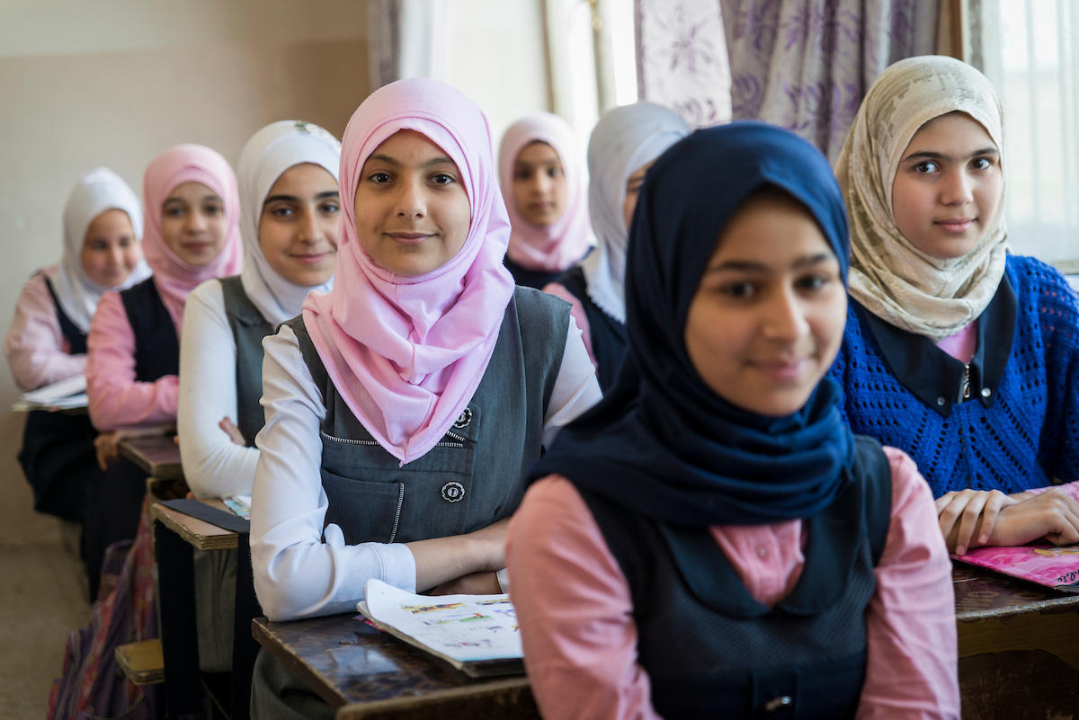 Several young women in hijabs sit at desks in a bright classroom.