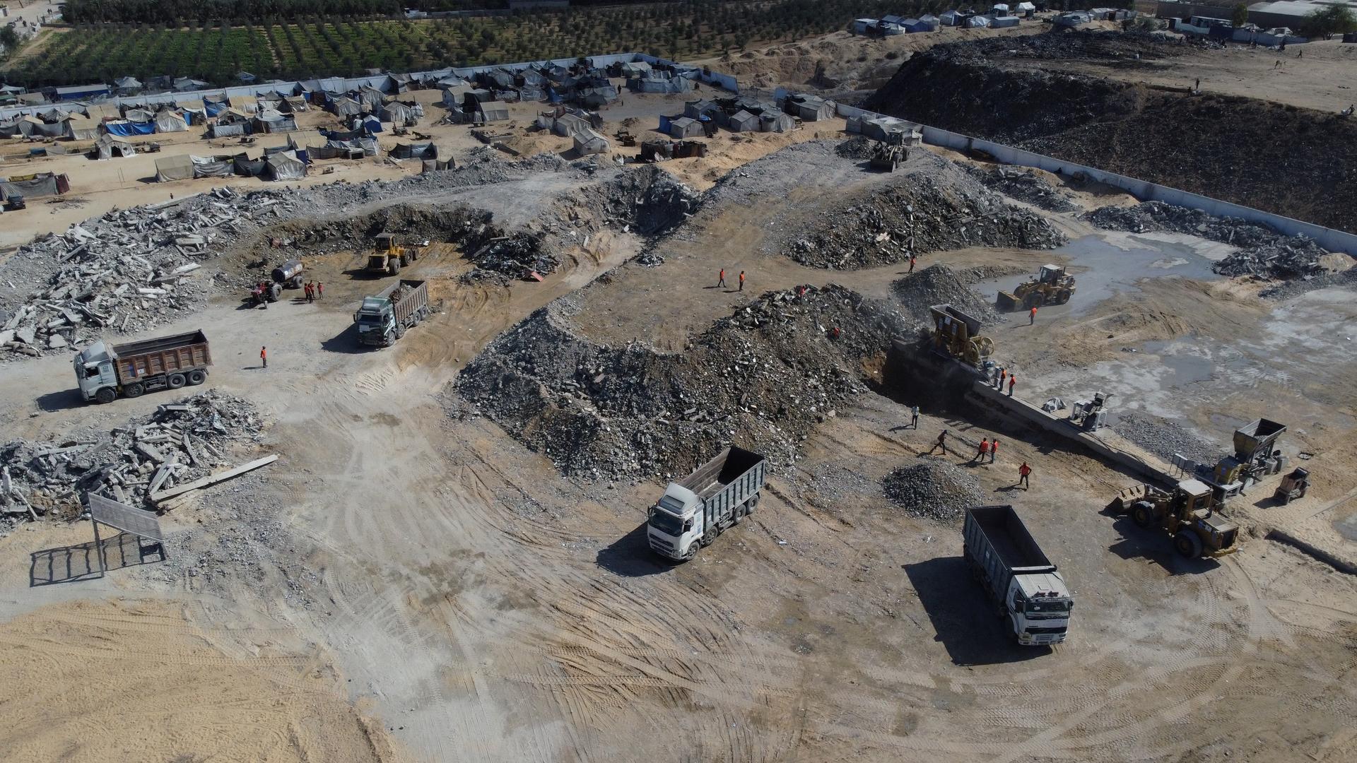 Aerial view of a dusty excavation site with dirt roads, parked trucks, and stone walls.