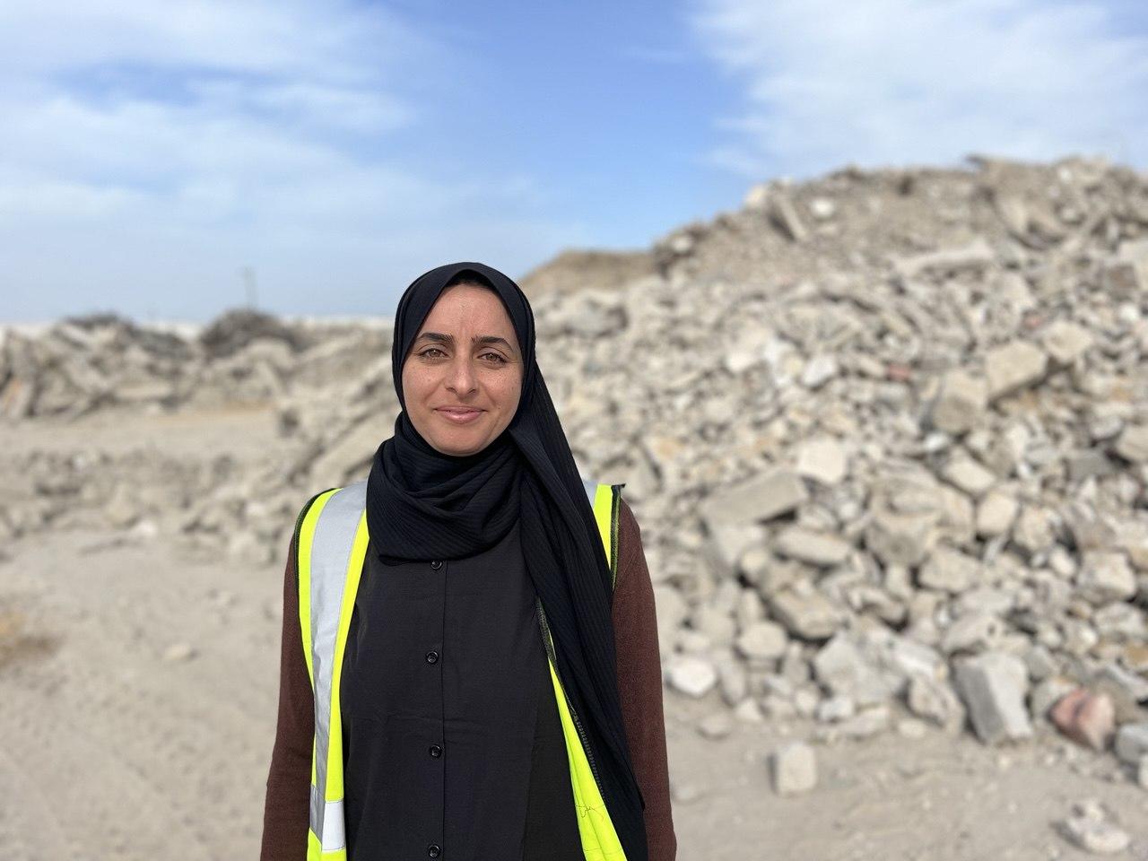 Person in black hijab and neon safety vest stands at a rocky quarry under a blue sky.