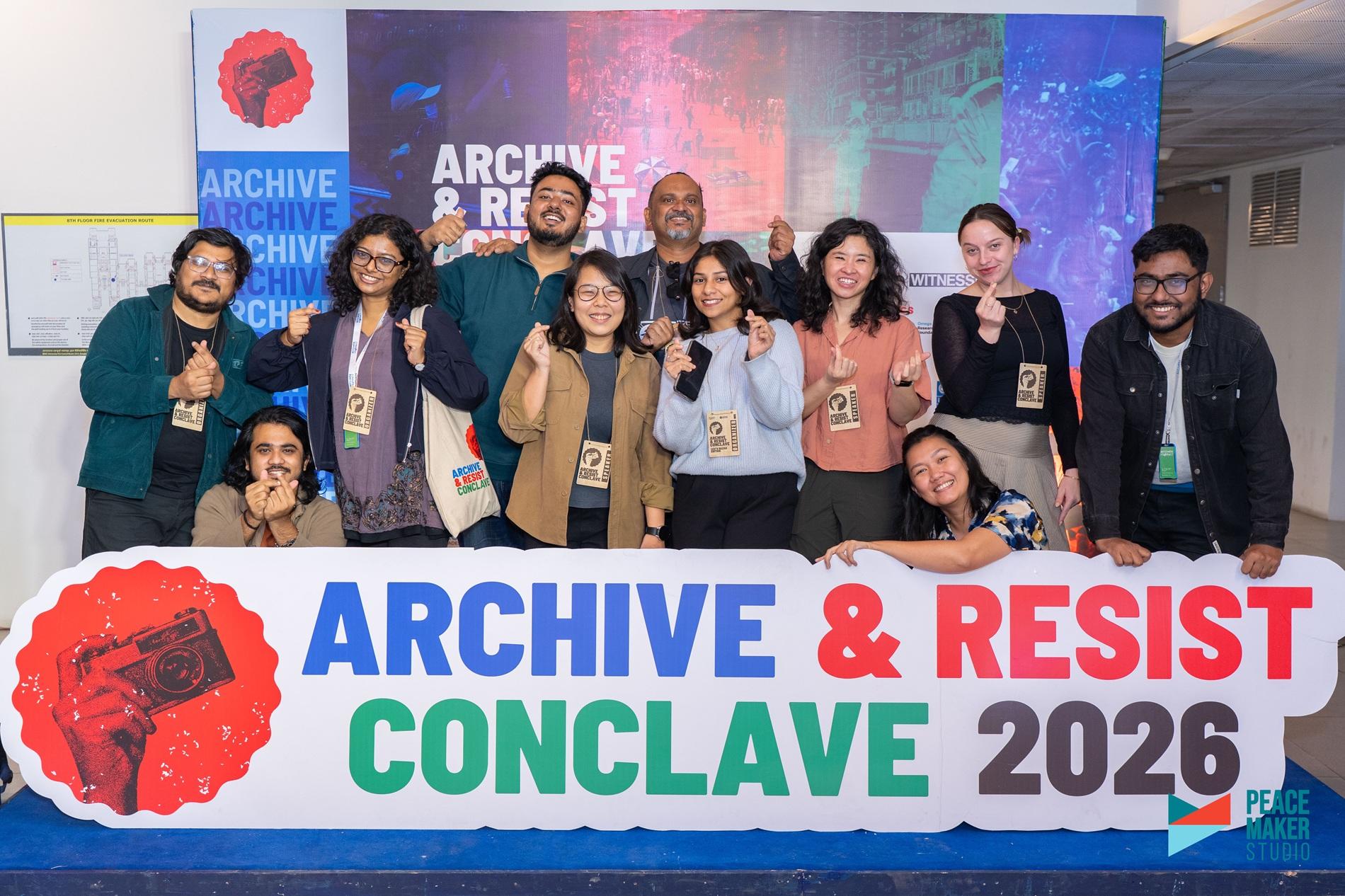 Group of diverse people posing on stage with a banner reading Archive & Resist Conclave 2026.