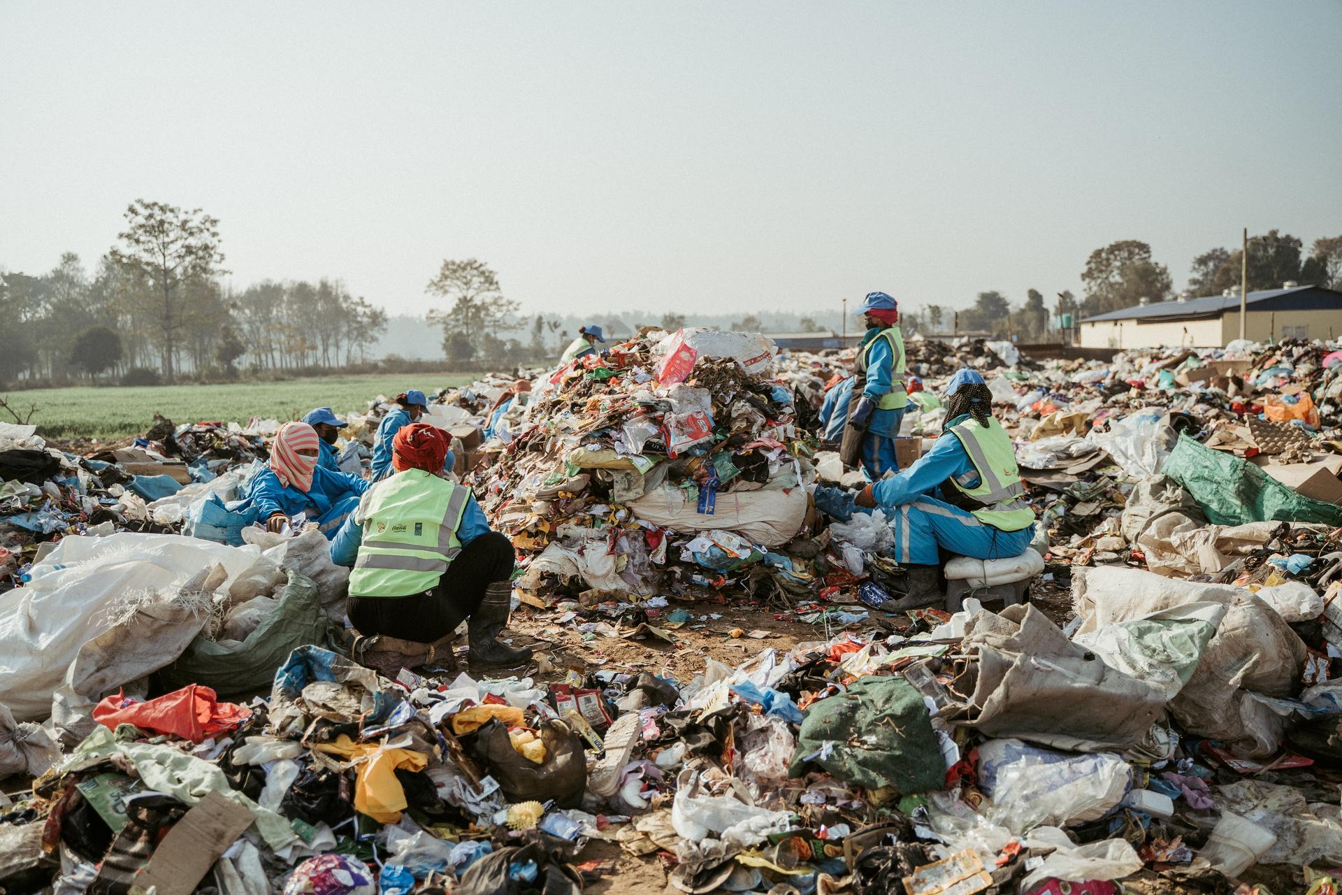 Outdoor scene of people sorting through a massive pile of garbage at a landfill.