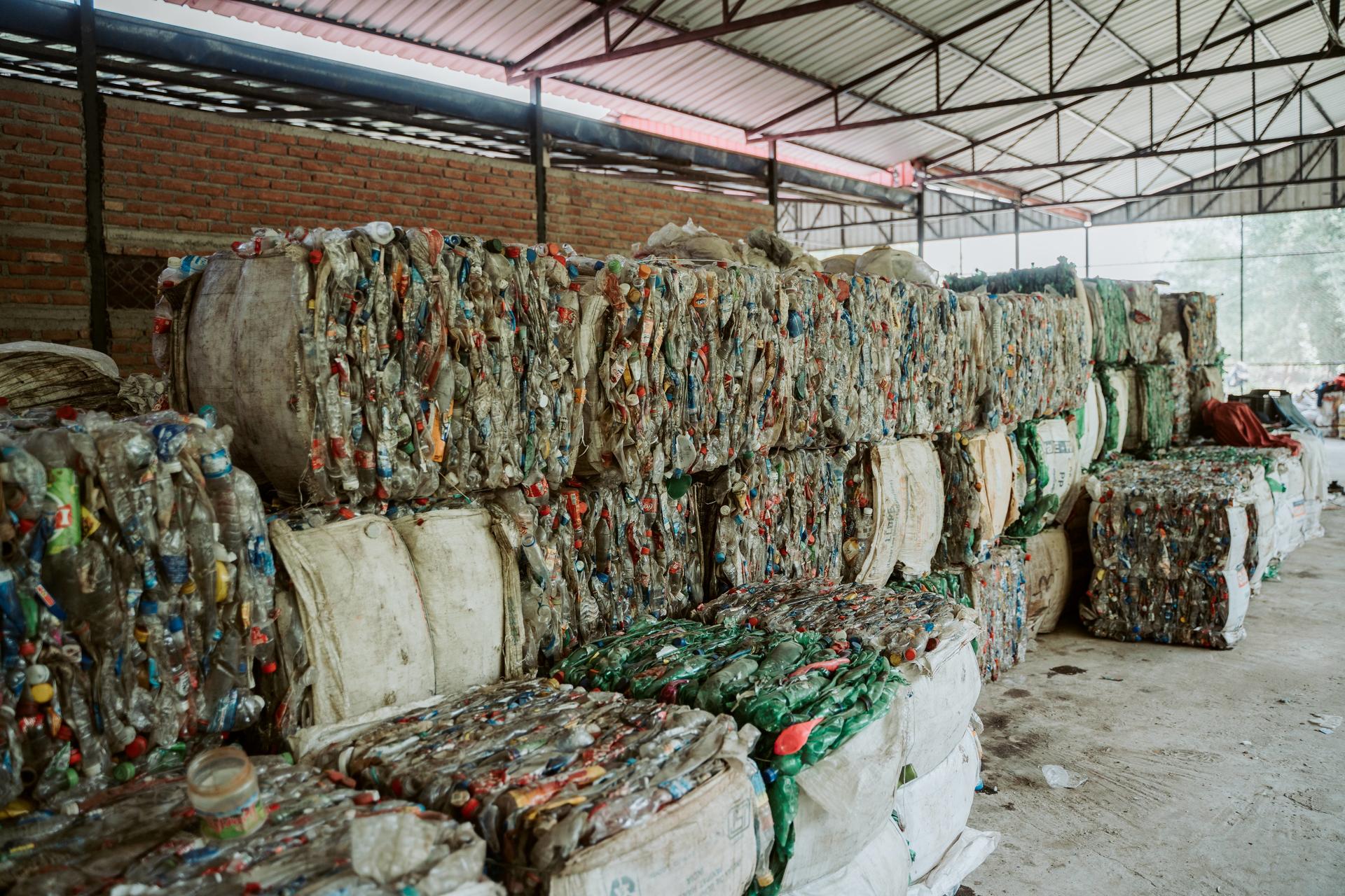 Indoor recycling plant with piled, compressed plastic bales wrapped in netting.