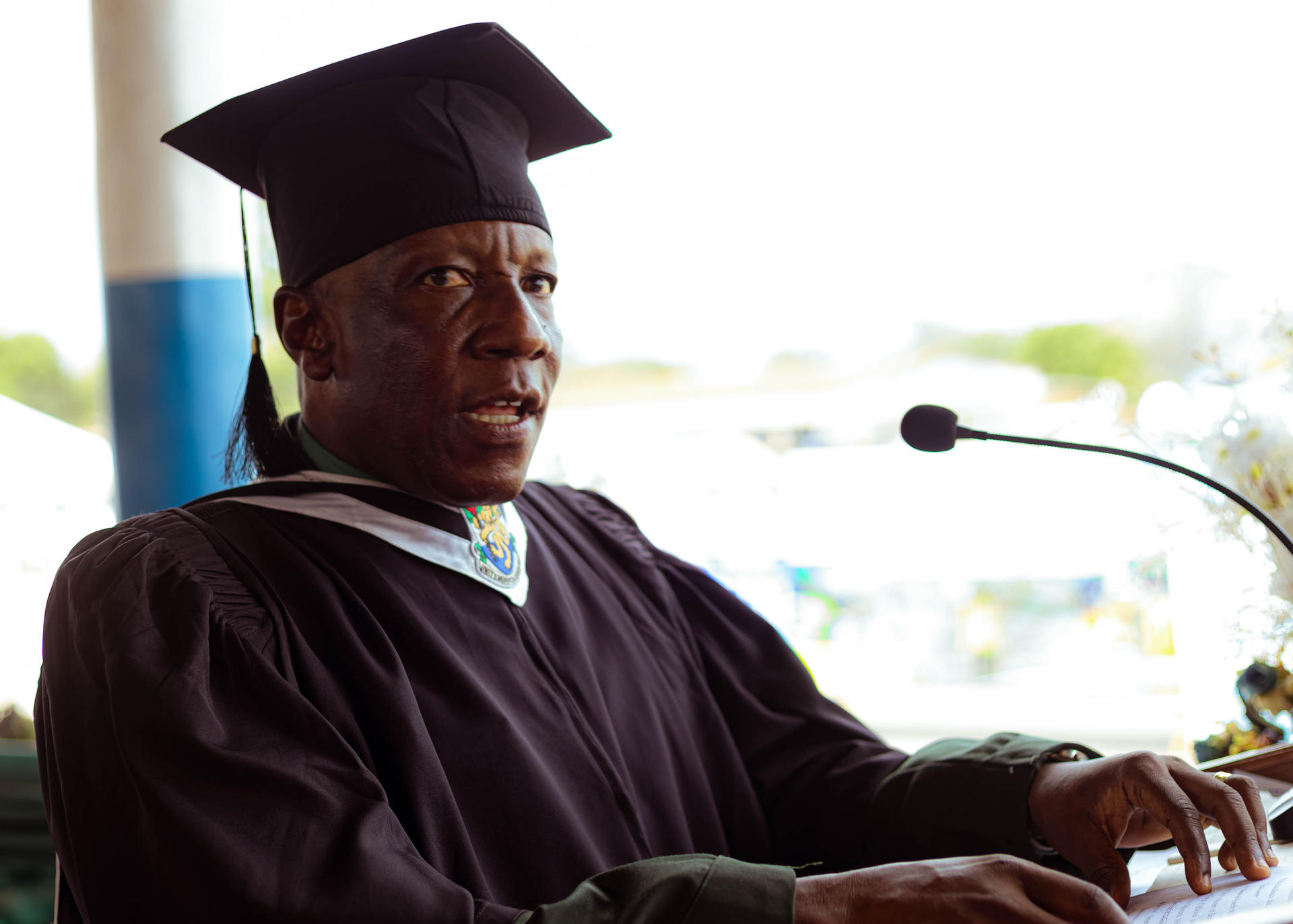 Photograph of a graduate speaking at a podium in a maroon gown and cap.