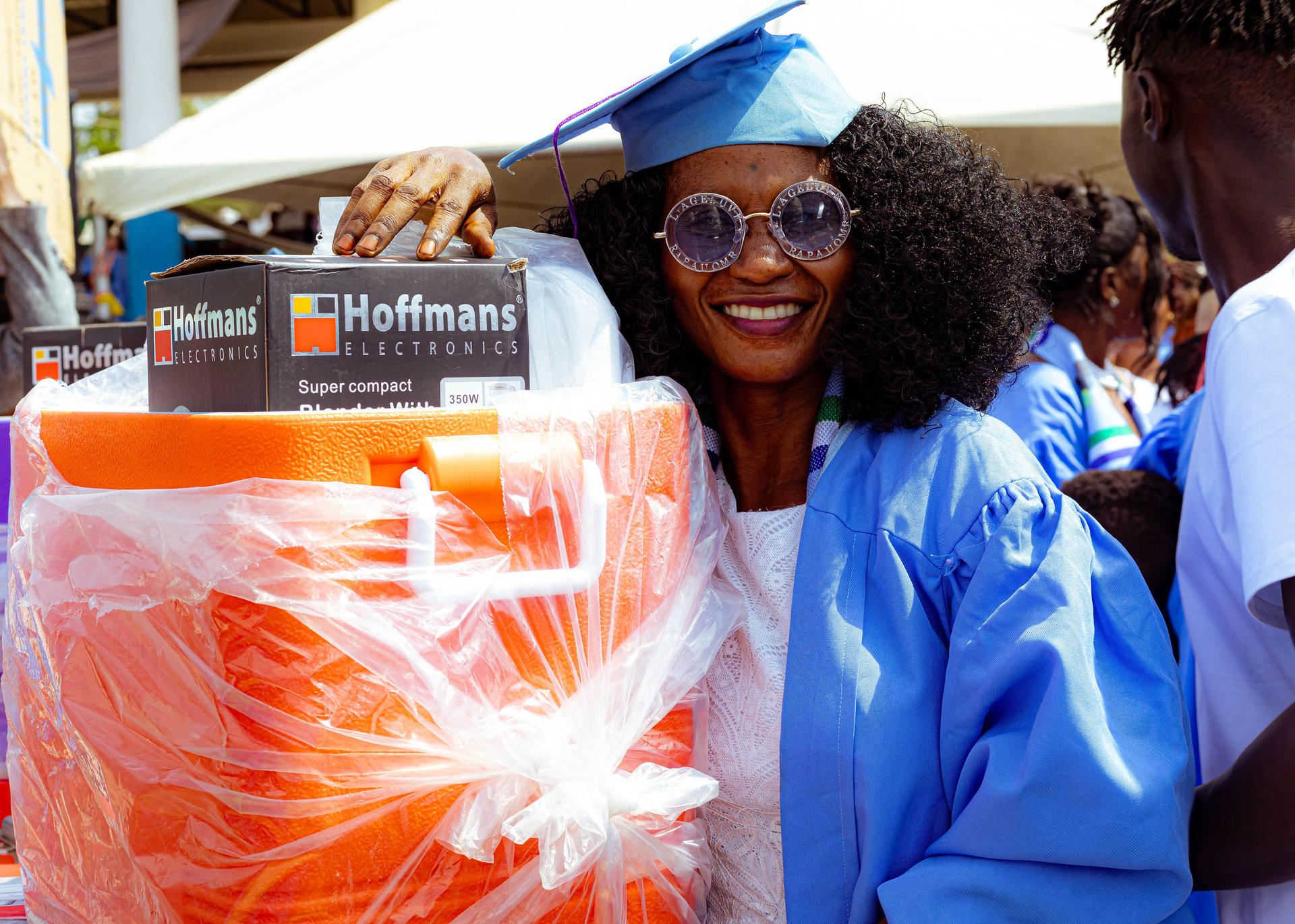 Market stall under a white canopy with an orange-wrapped bundle and blue-clad people.