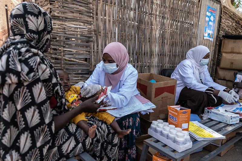 Outdoor market scene with women in hijabs at a table sorting eggs; egg cartons and boxes.