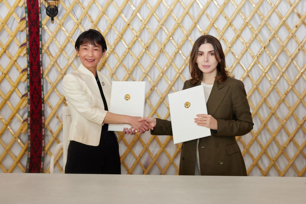 Two women in business attire hold certificates during a ceremony in front of a gold lattice backdrop.
