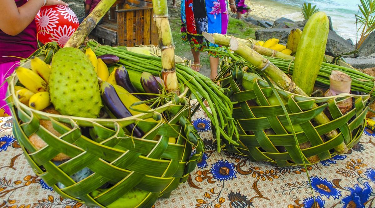 Two green palm-leaf baskets filled with tropical fruits on a patterned tablecloth.