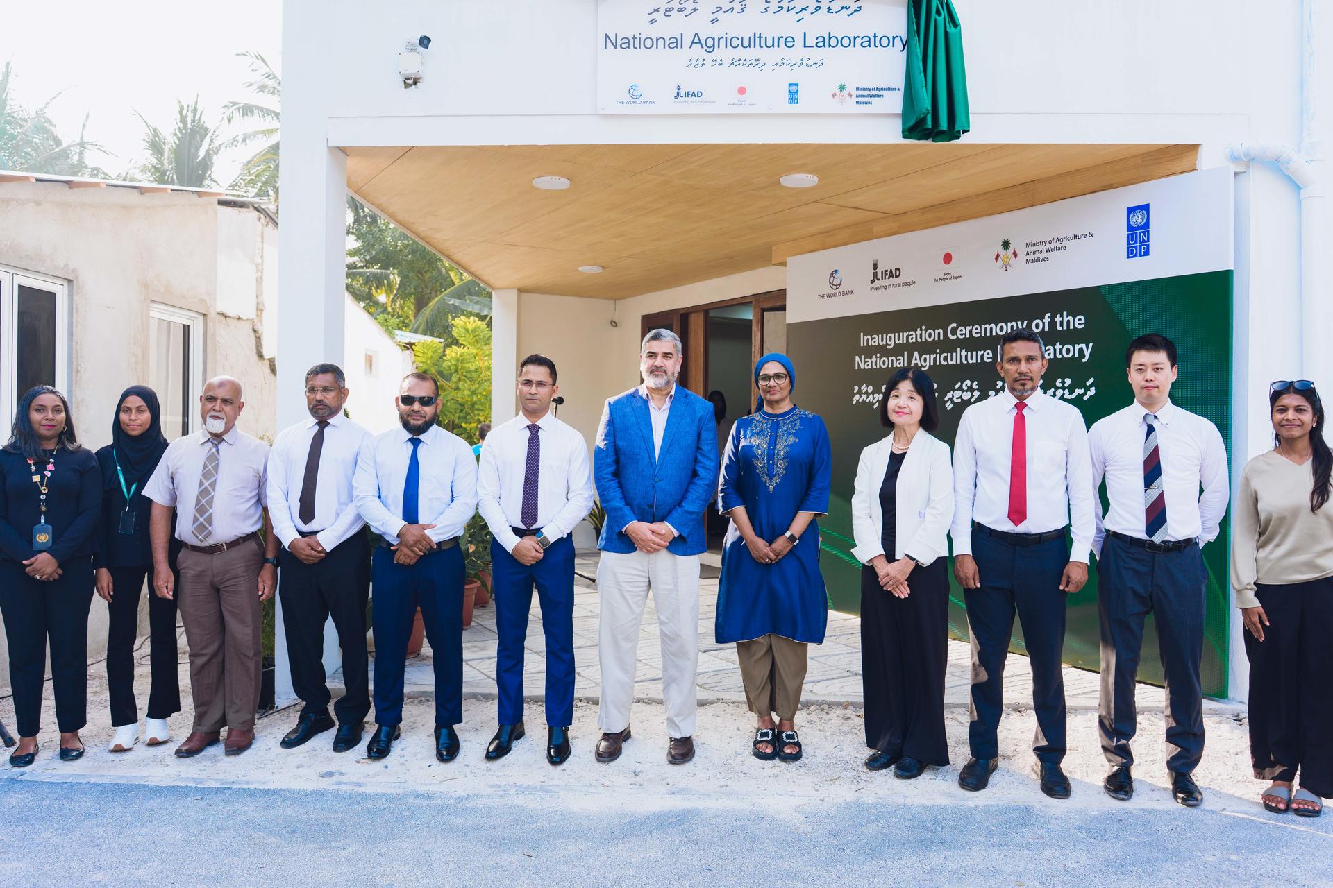 Group photo: people in business attire posing in front of a building with banners.