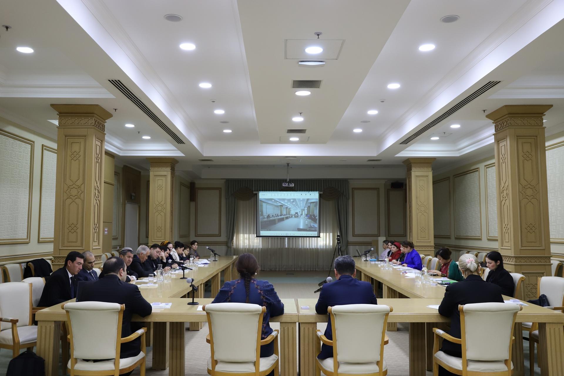 Photograph of a formal boardroom meeting around a table with ornate columns and projector screen.