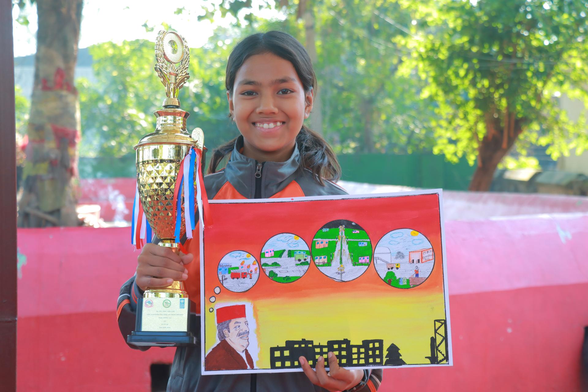Photograph of a person outdoors holding a tall trophy and a colorful display board.