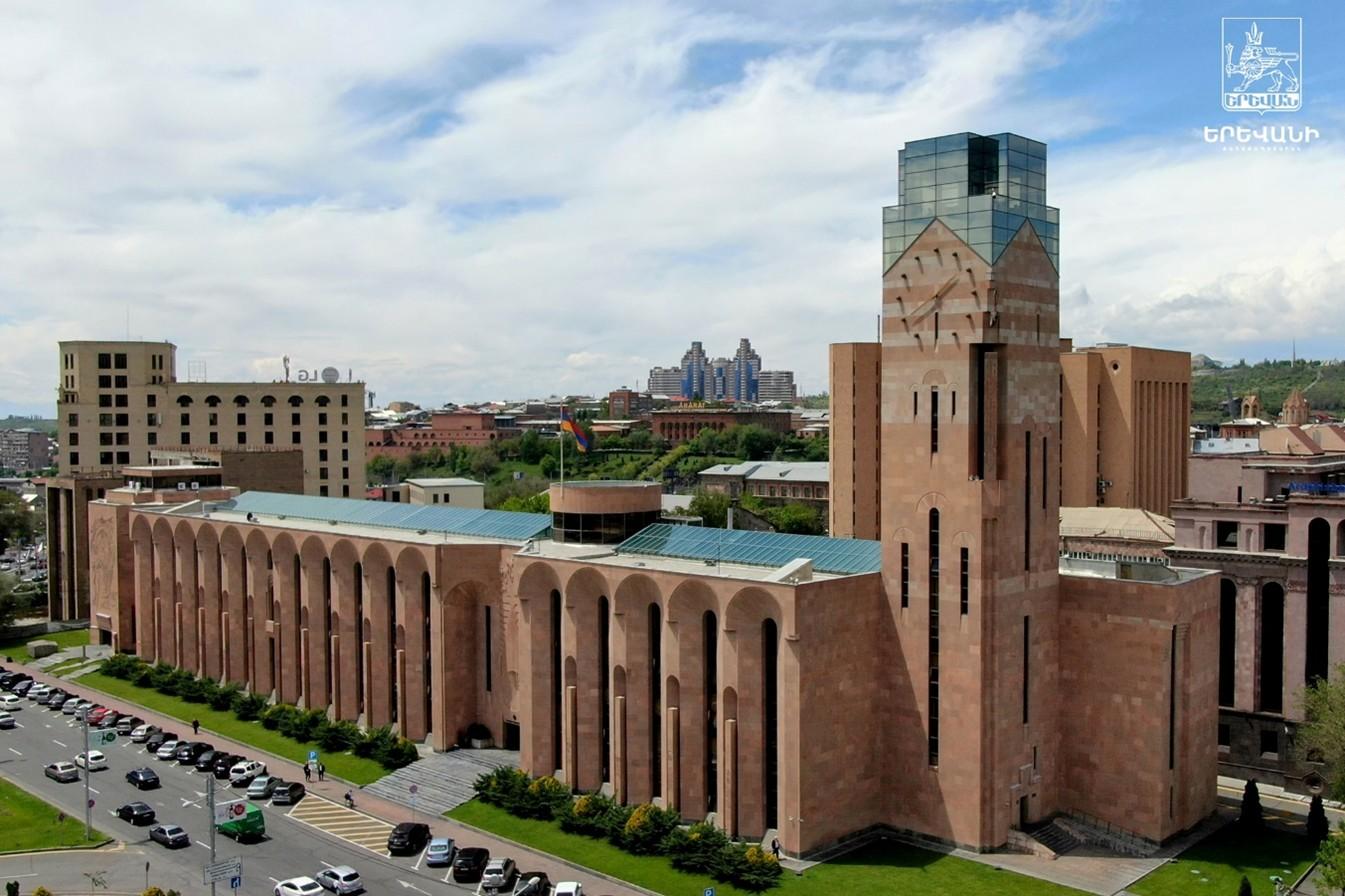 Brick university building with a tall central tower and long arched colonnade on a sunny day.