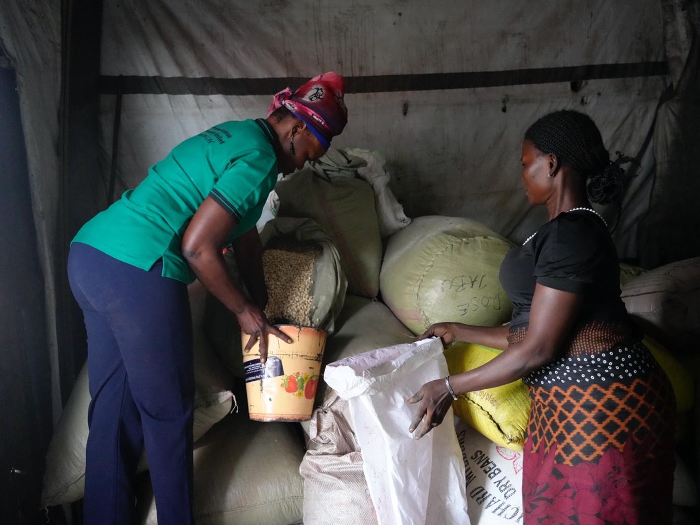Two women in a small room handling large sacks of grain.