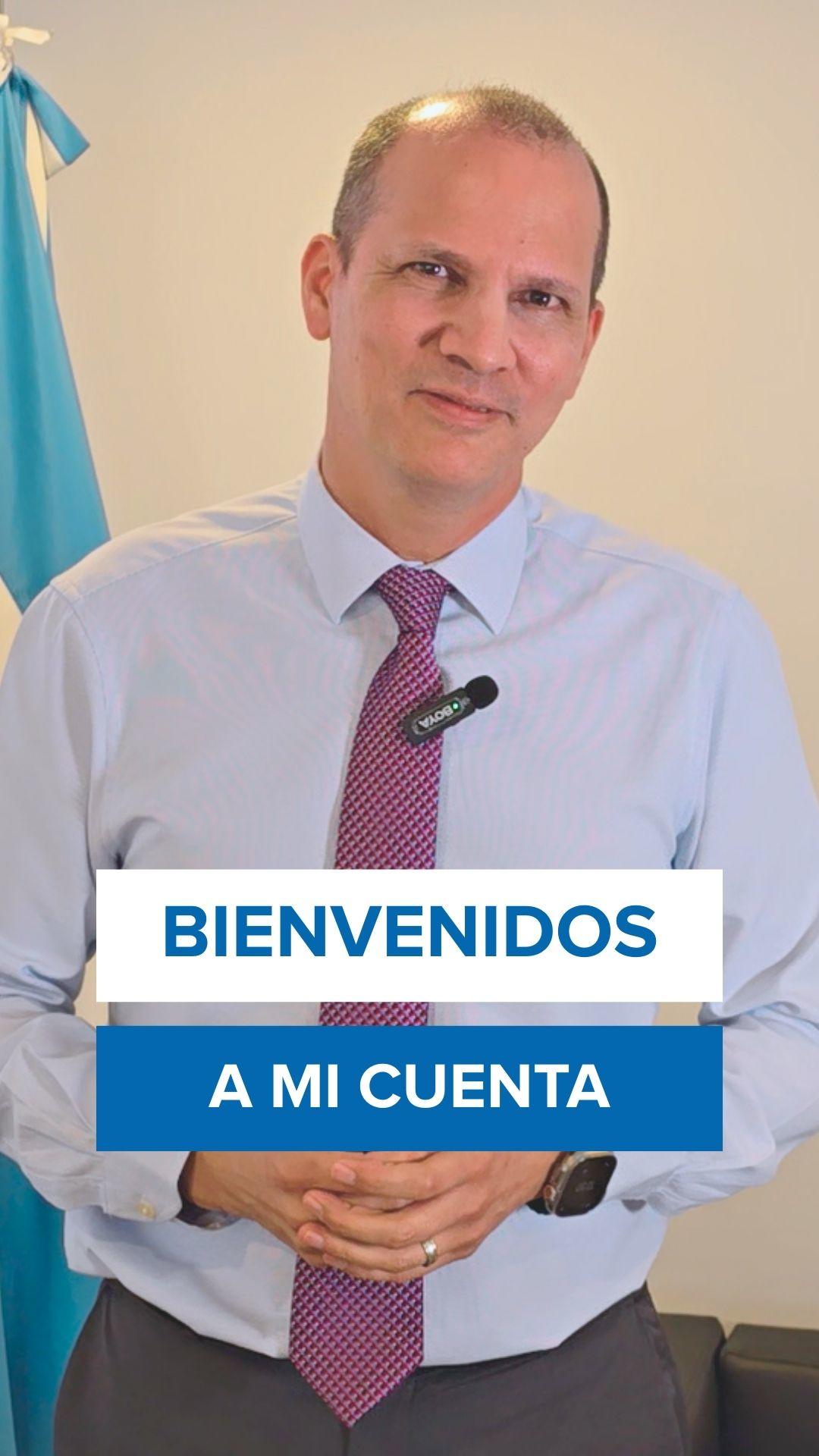 Presenter in white shirt and purple tie with microphone, blue flag beside; BIENVENIDOS A MI CUENTA banner.