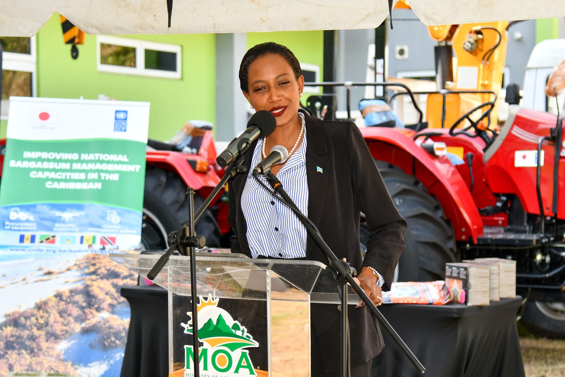Speaker at a podium with microphone at an agricultural event; red tractors in the background.