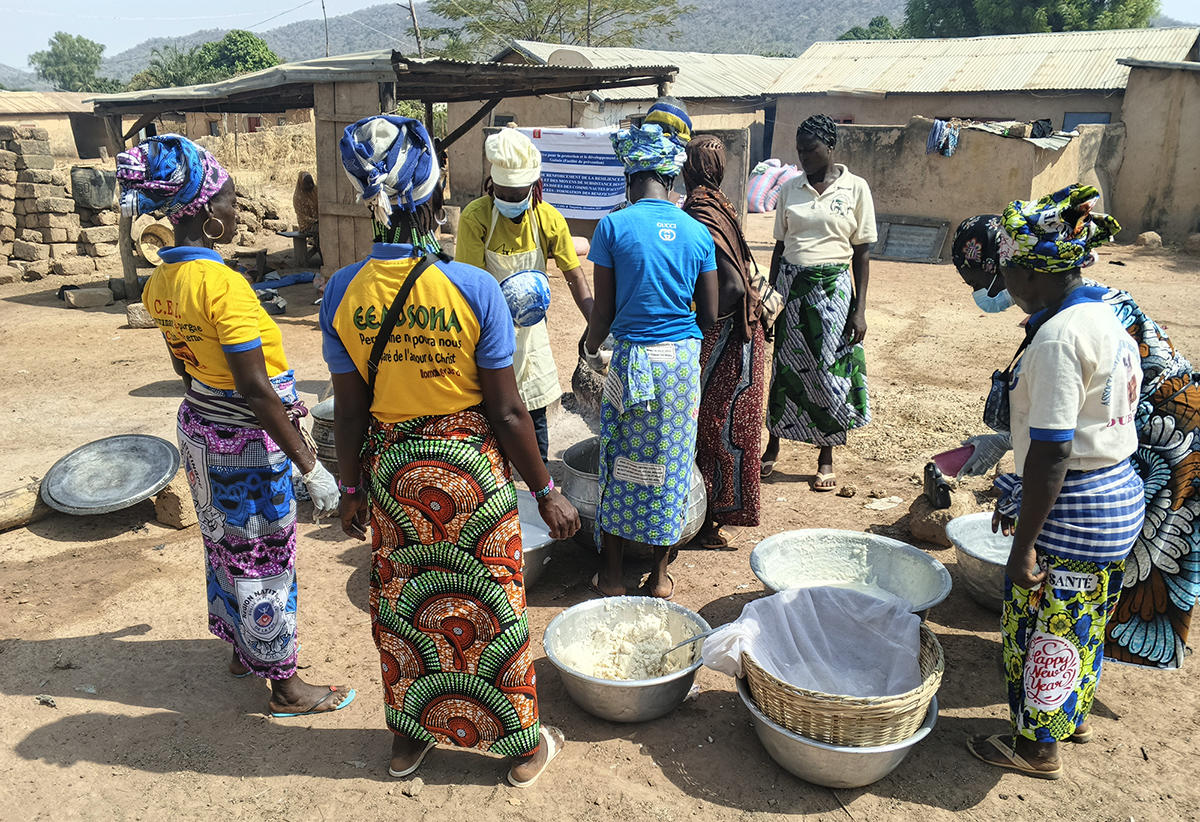 Photo of villagers, mostly women in colorful wraps, gathered around outdoor pots.