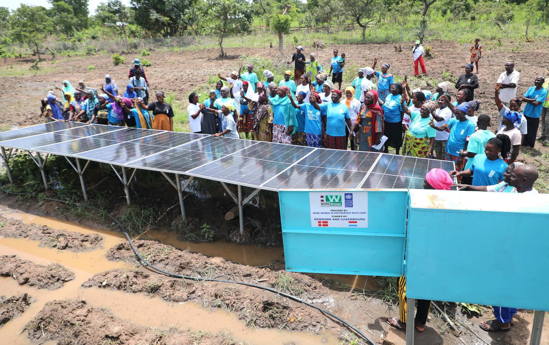 Group of people in blue shirts gathered around solar-powered water pump and blue tanks.