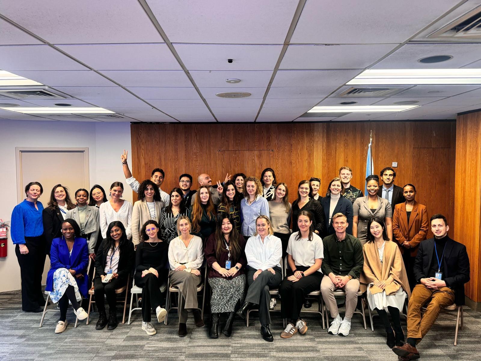 Large diverse group of professionals smiling in a conference room with a wood-paneled wall.