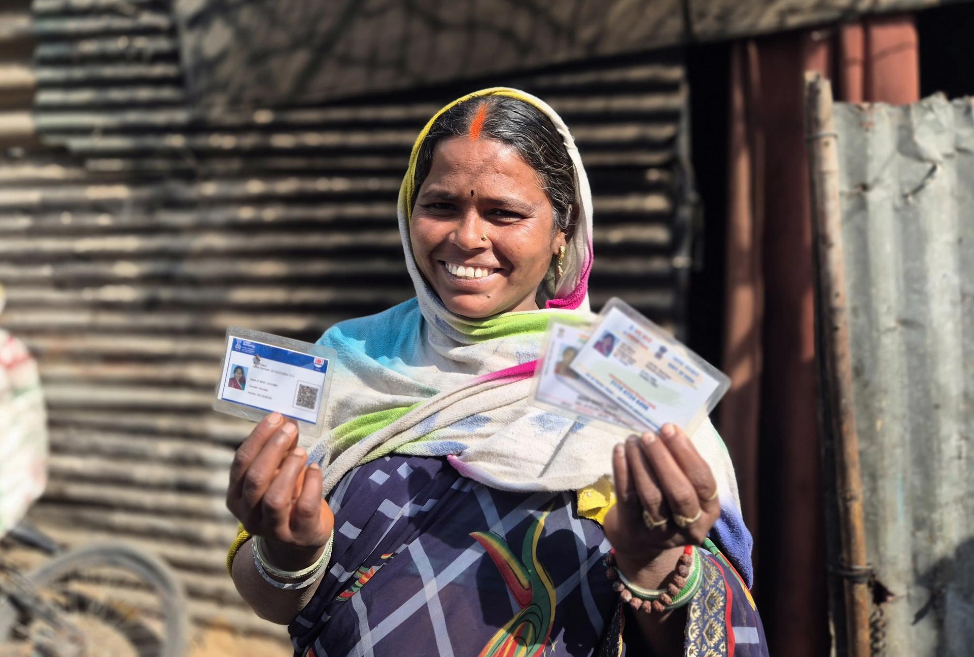 Person in colorful clothing and headscarf holds several banknotes in a gritty alley.