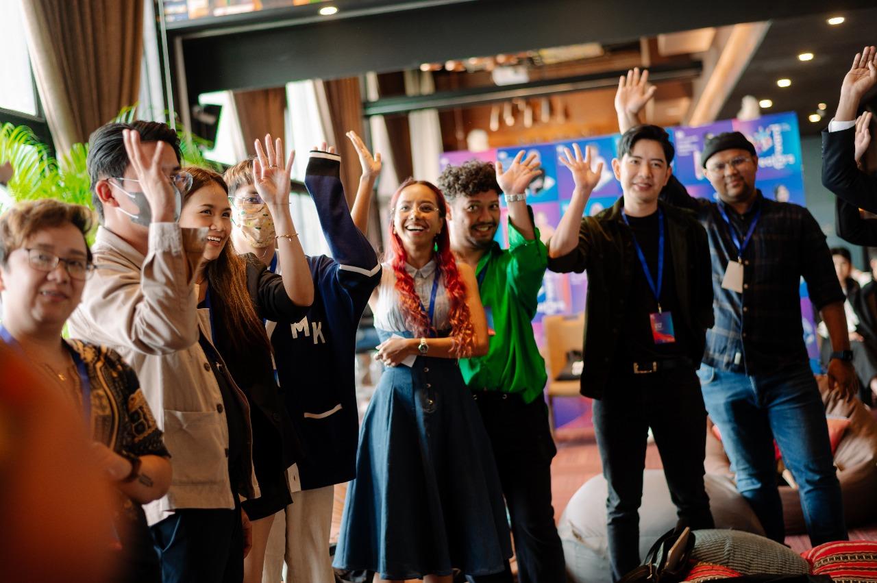 Diverse group of conference attendees posing for a group photo with hands raised.