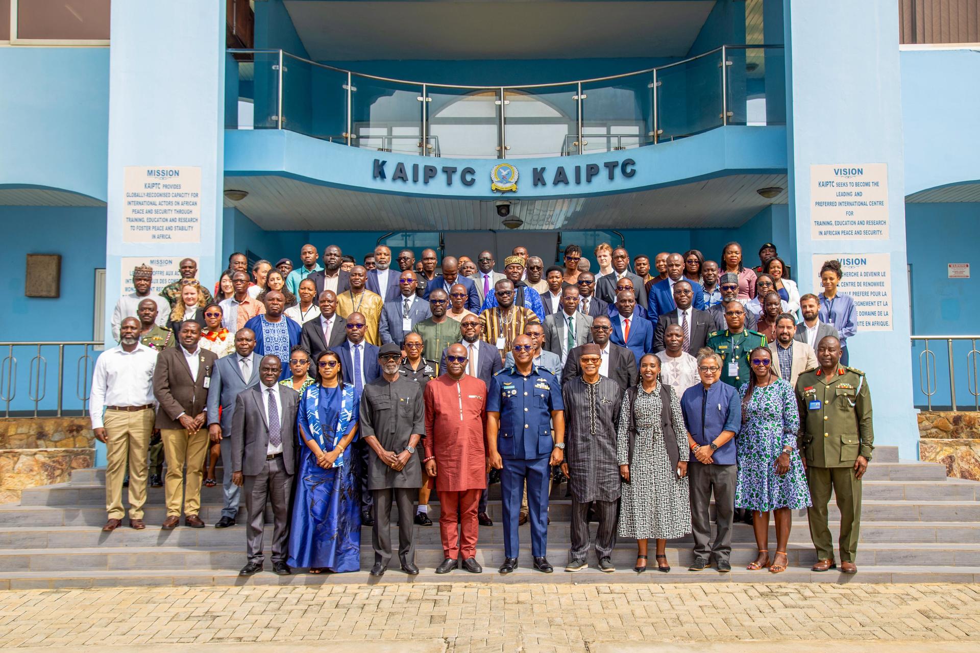 Photograph of a large group gathered on steps in front of a blue building with a banner.