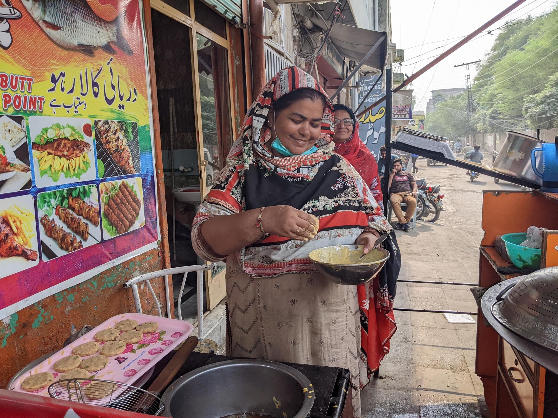 Woman in headscarf serves fried food on a plate at a street market stall.