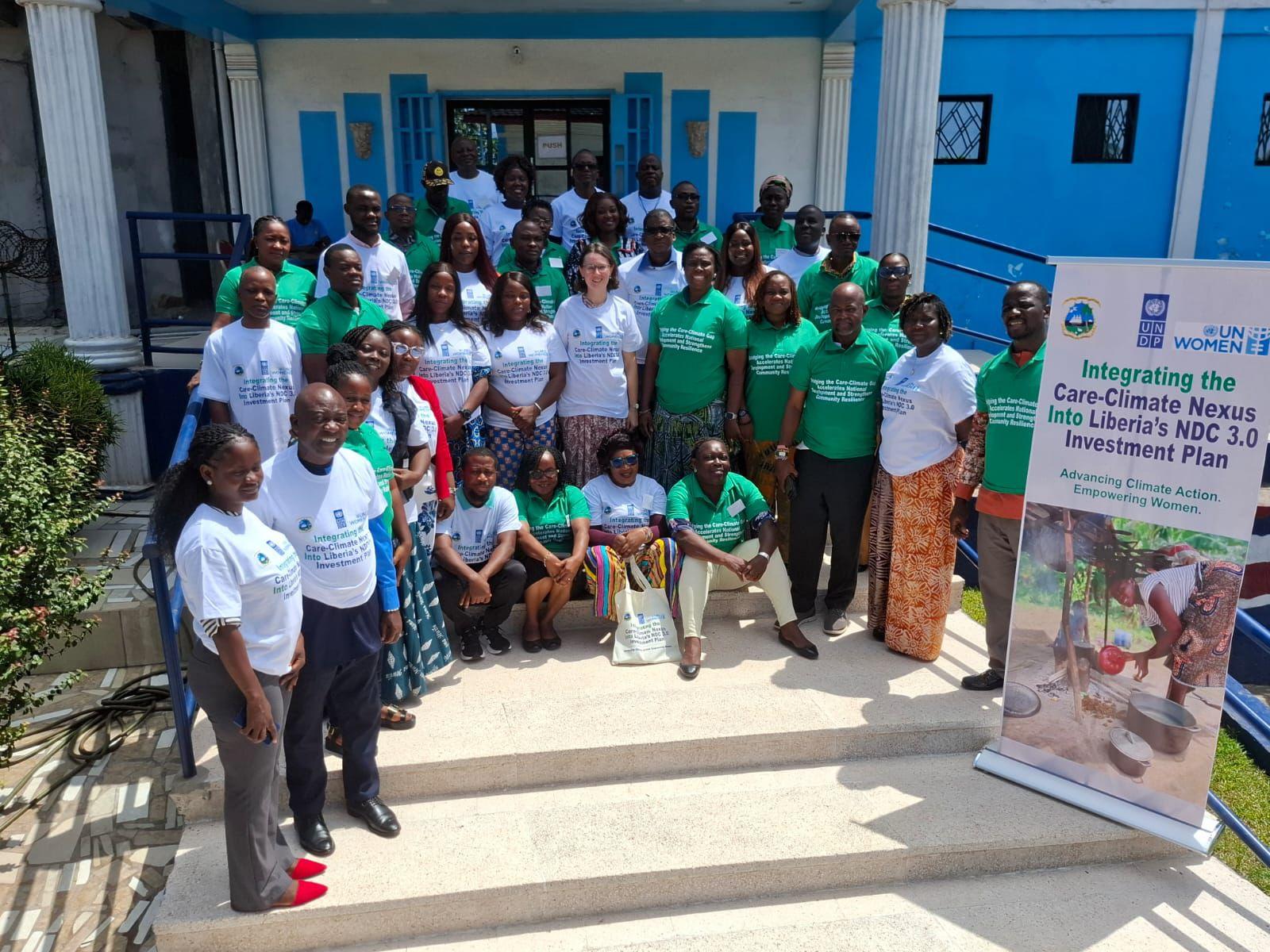 Group of people in white shirts posing on steps outside a blue building; banner to the right.