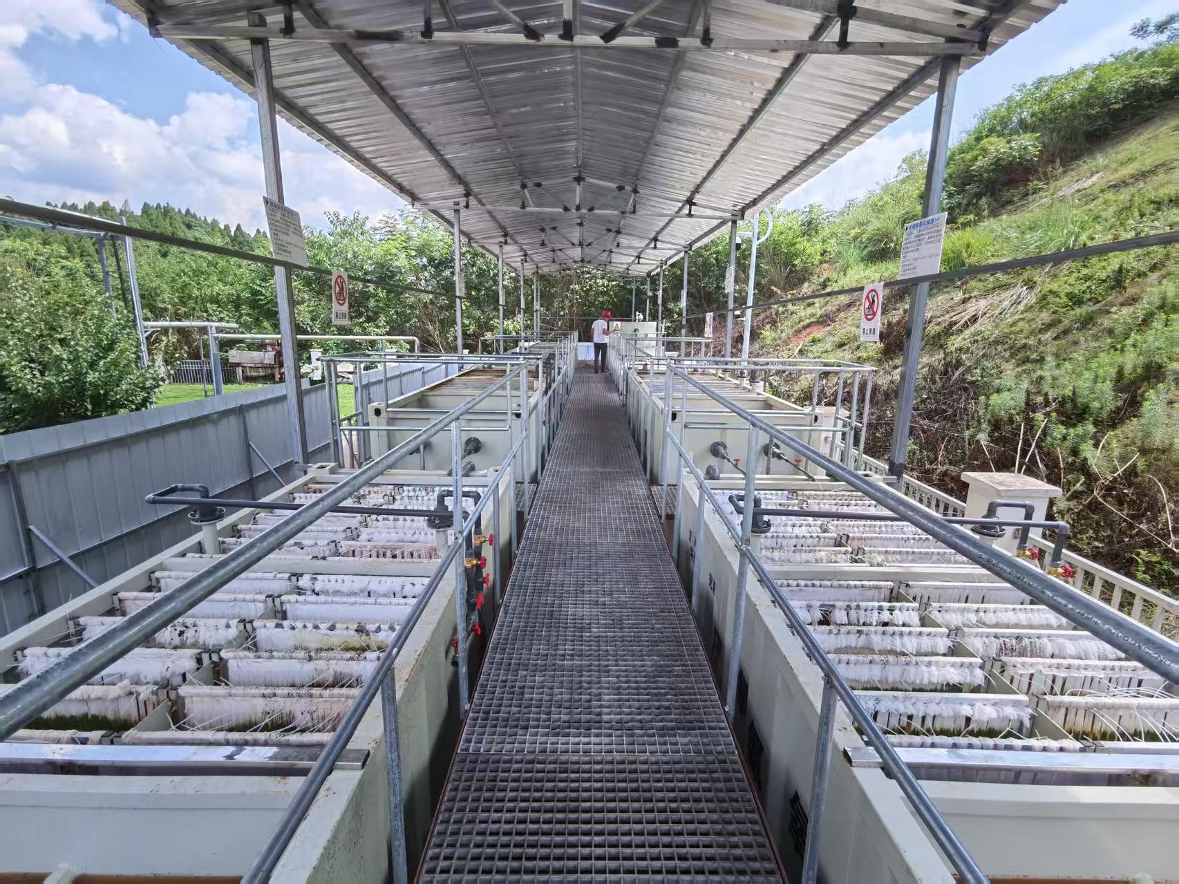 Open-air aquaculture facility with long rows of rectangular water tanks along a central grated walkway.