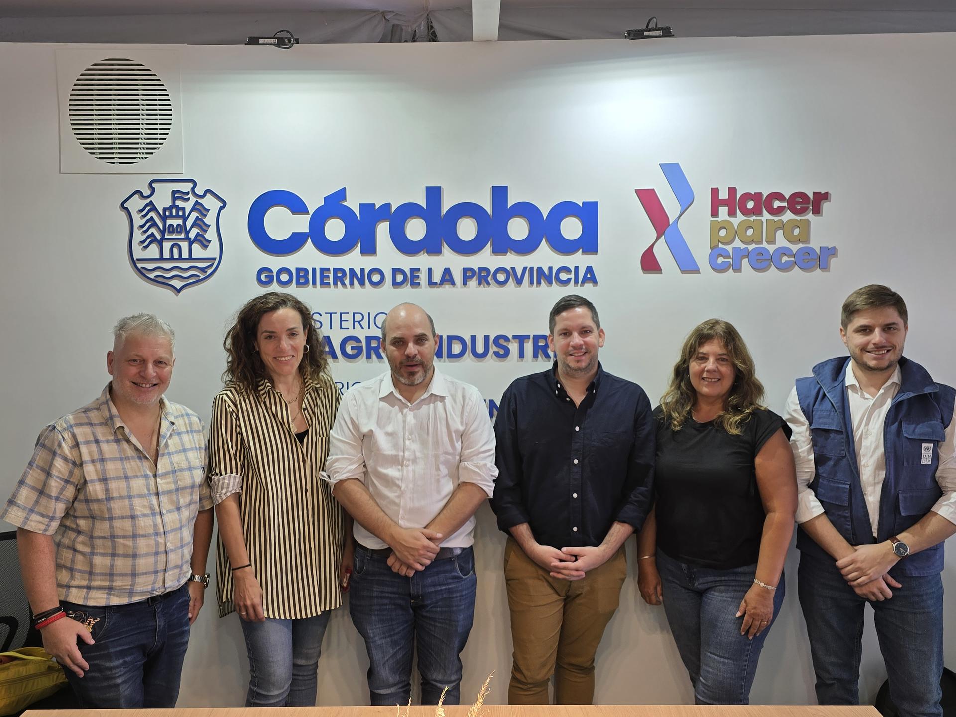 Seven adults posing in front of Córdoba provincial government banners.